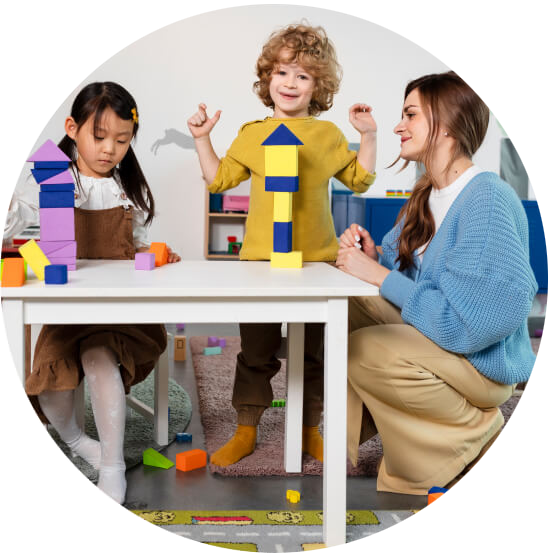 A young girl and an adult woman playing with colorful building blocks at a white table in a playroom.