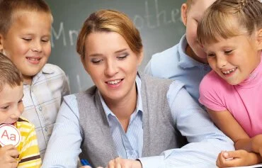 Teacher leading a classroom activity with young students gathered around her at a desk.