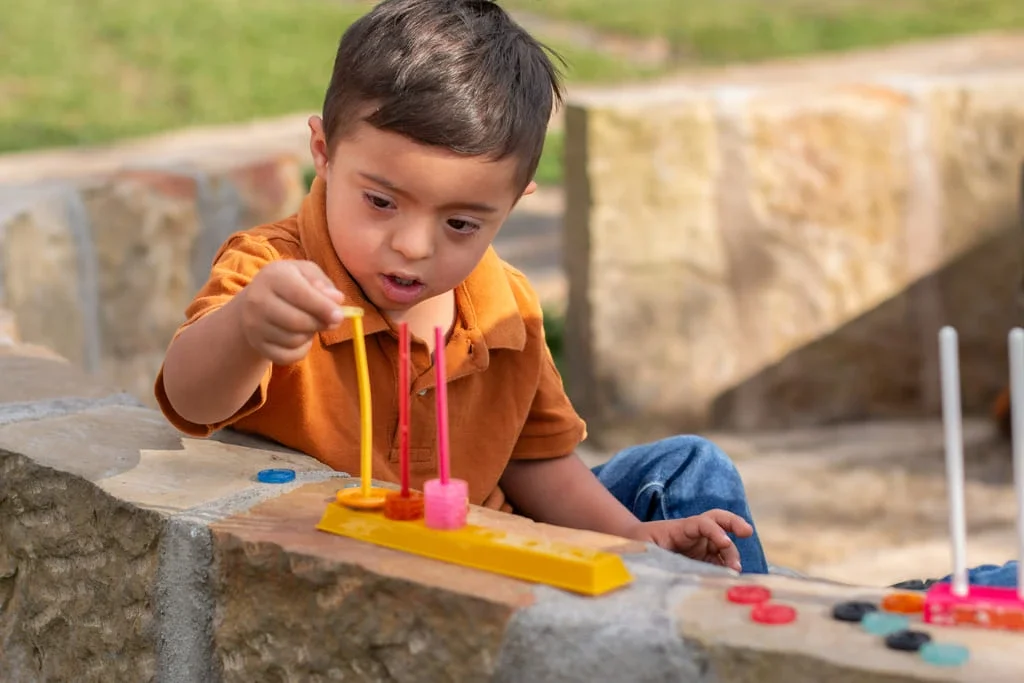 A young boy playing the game Connect 4 outdoors on a stone ledge.
