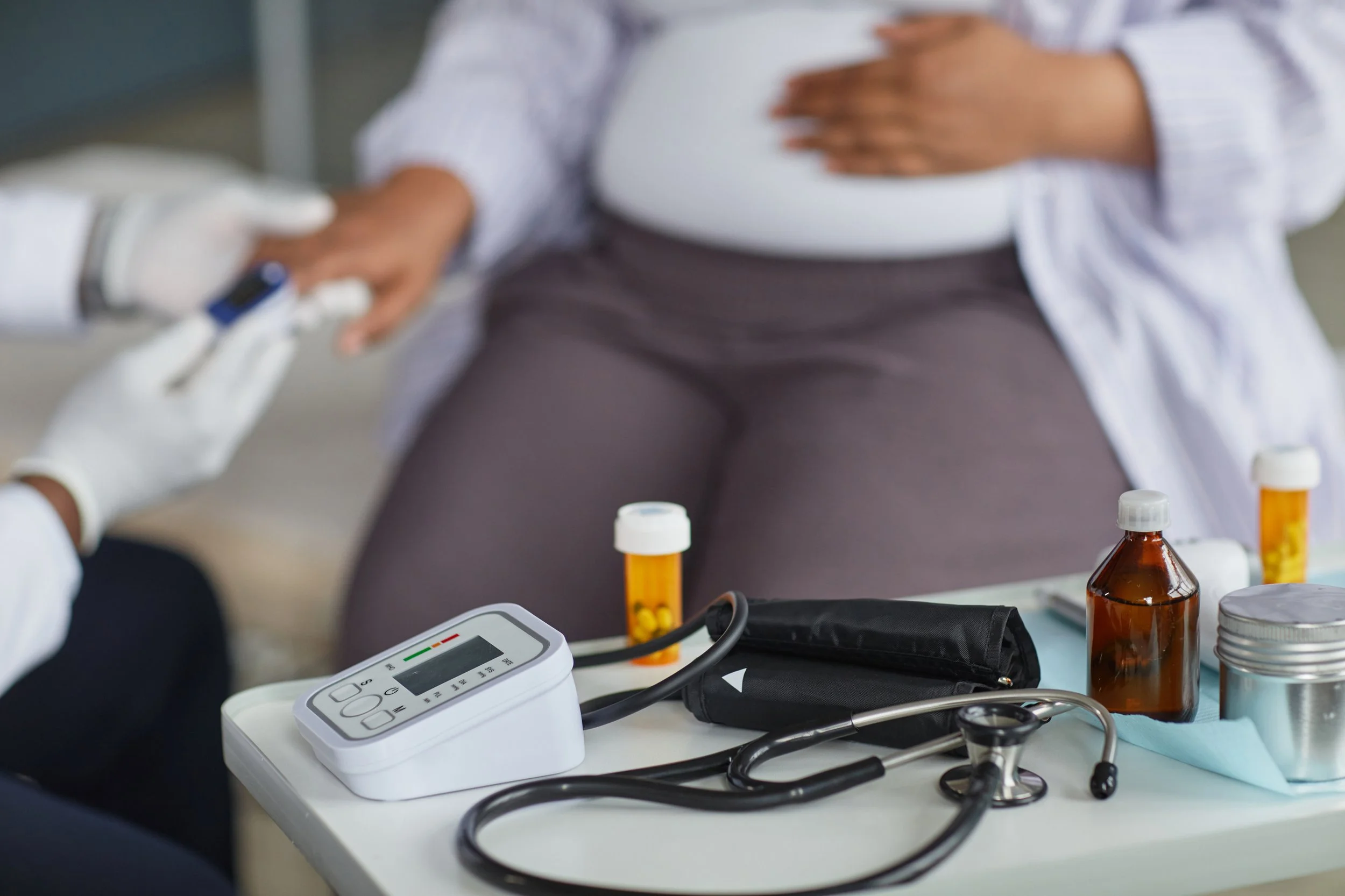 A person receiving a medical injection while seated at a table with medical supplies, including bottles, a blood pressure monitor, and a stethoscope, in what appears to be a clinical setting.