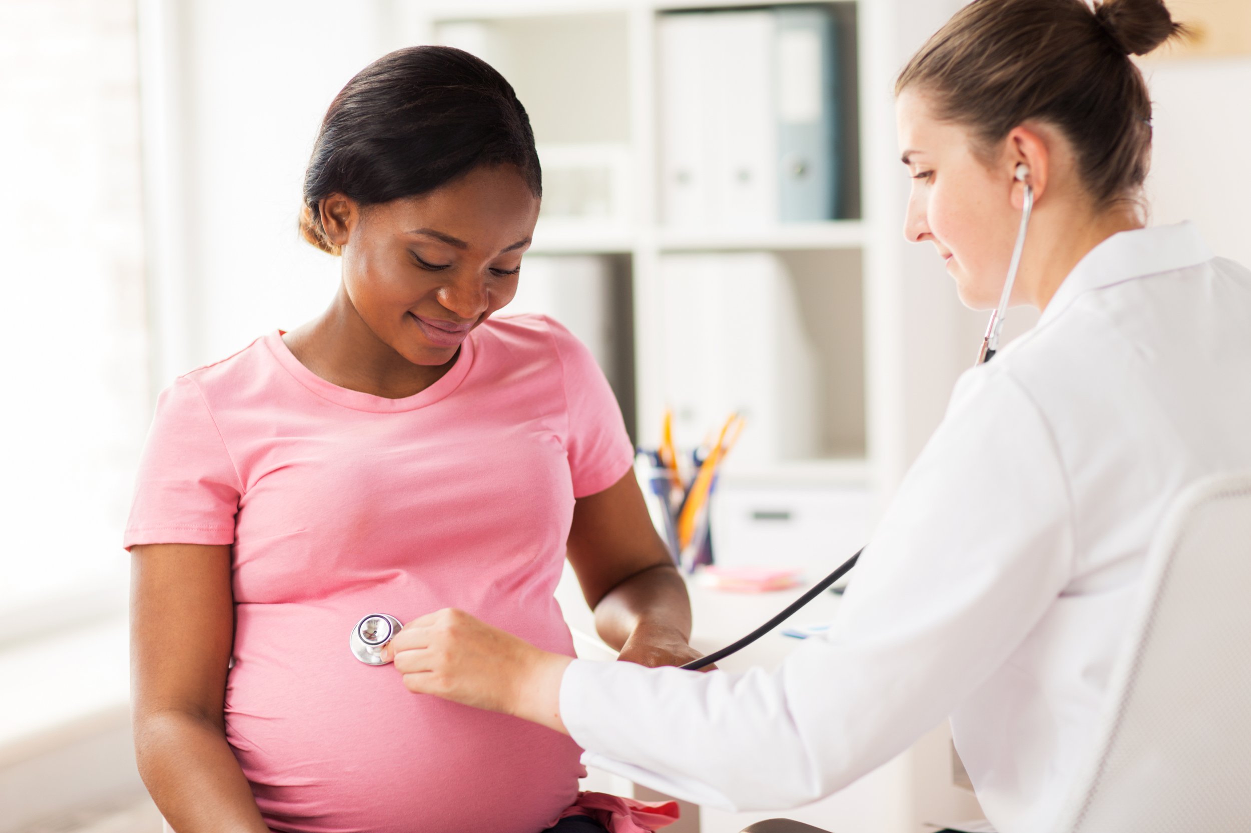 A healthcare professional checks a pregnant woman's blood pressure using a sphygmomanometer in a clinical setting.