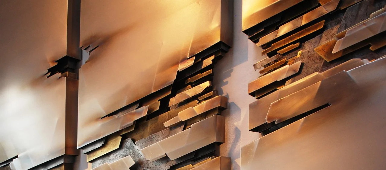 Close-up of a metallic abstract sculpture with stacked, irregularly-shaped metal pieces in bronze and copper tones.