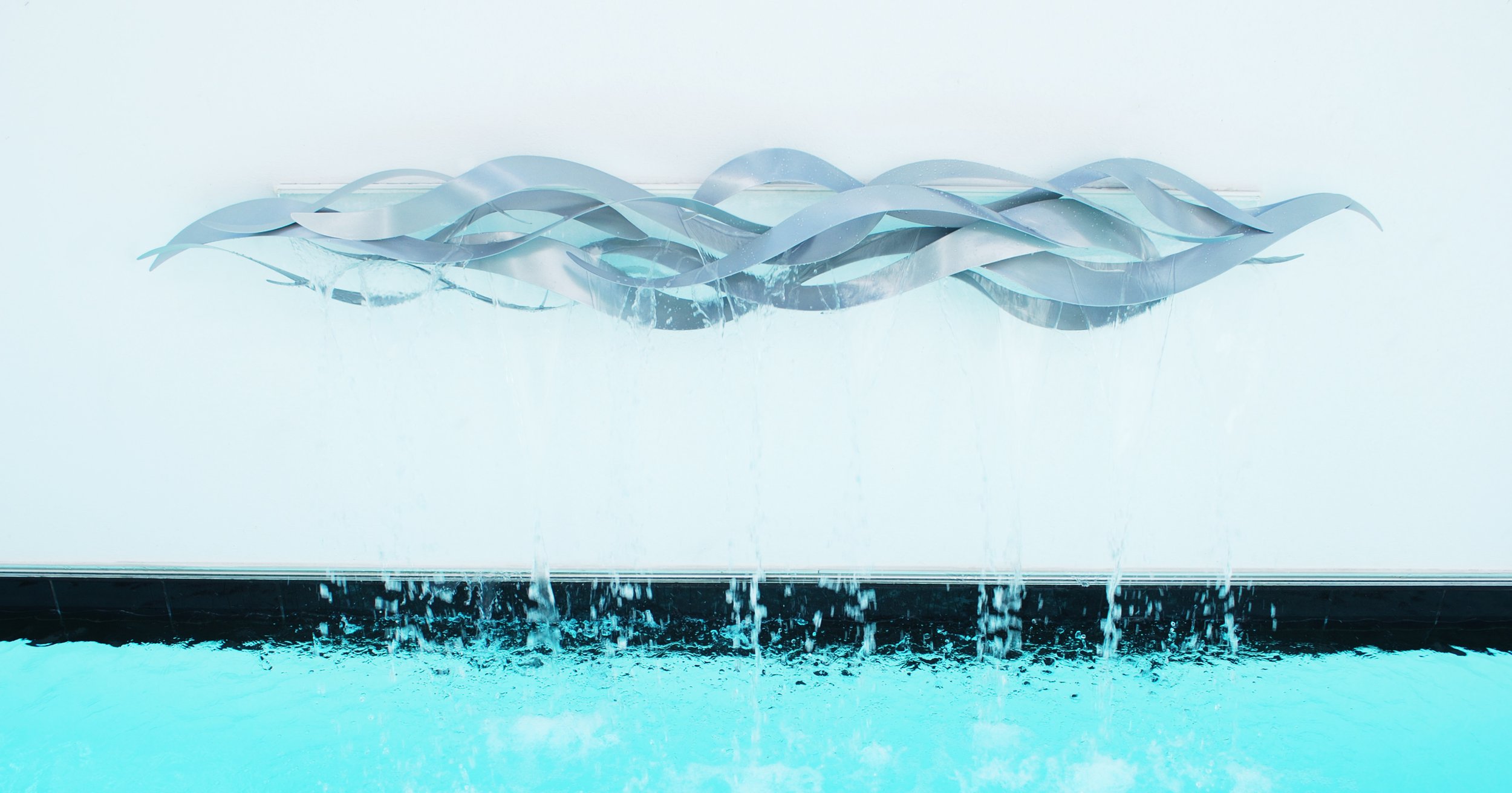 Modern wall decoration with twisted metallic ribbons hanging above a water feature with small waterfalls.