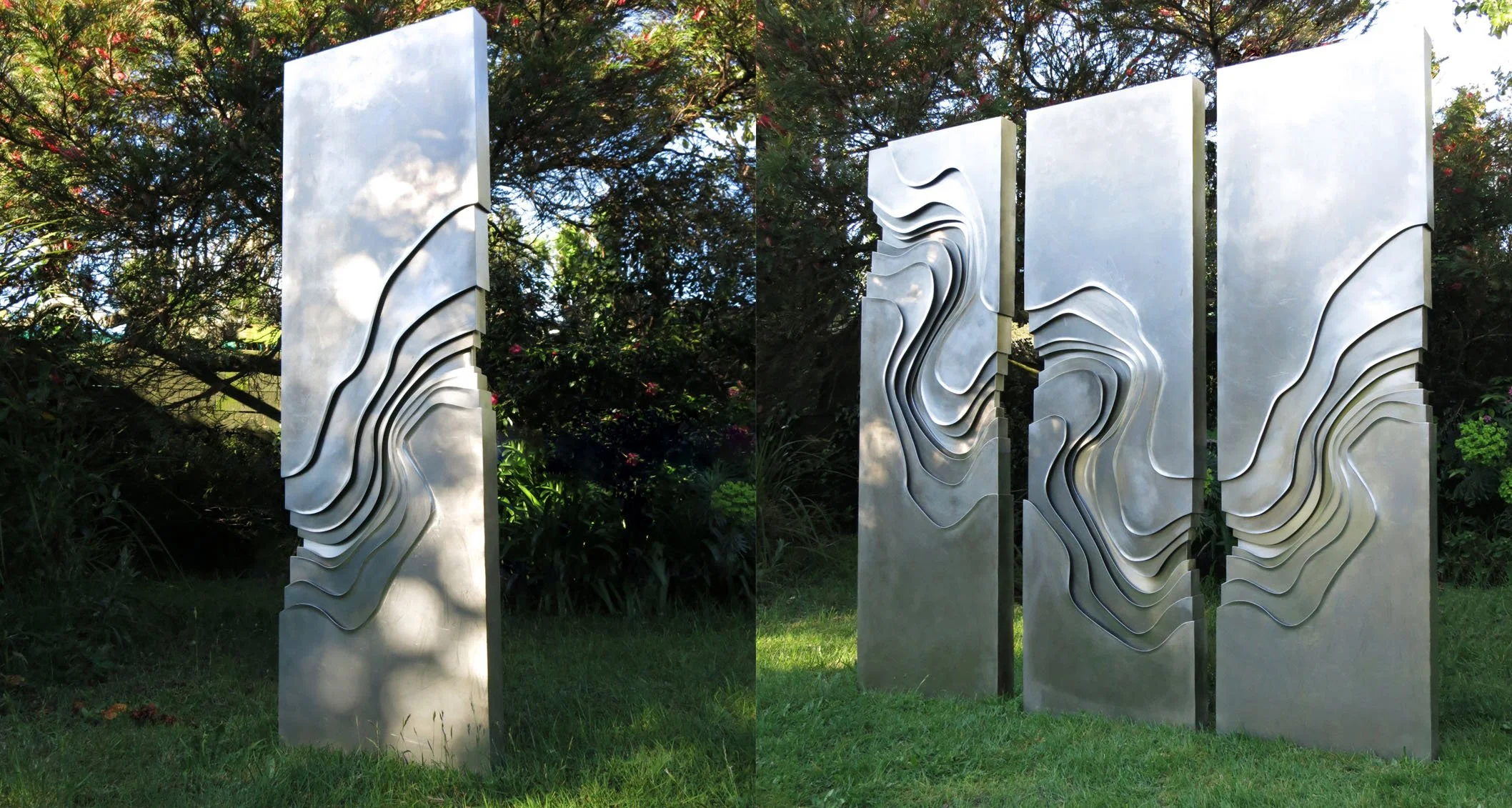 Set of three vertical metal sculptures outdoors, each with wavy, layered designs, set against a backdrop of trees and grass.