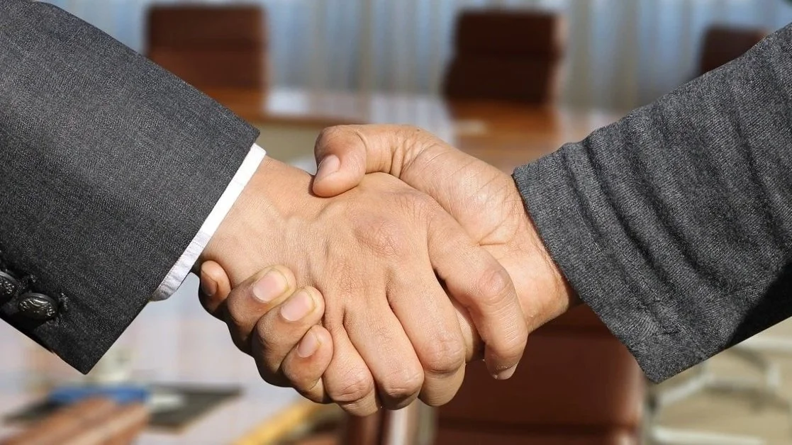 Close-up of a handshake between two individuals, one wearing a suit, in a professional setting.