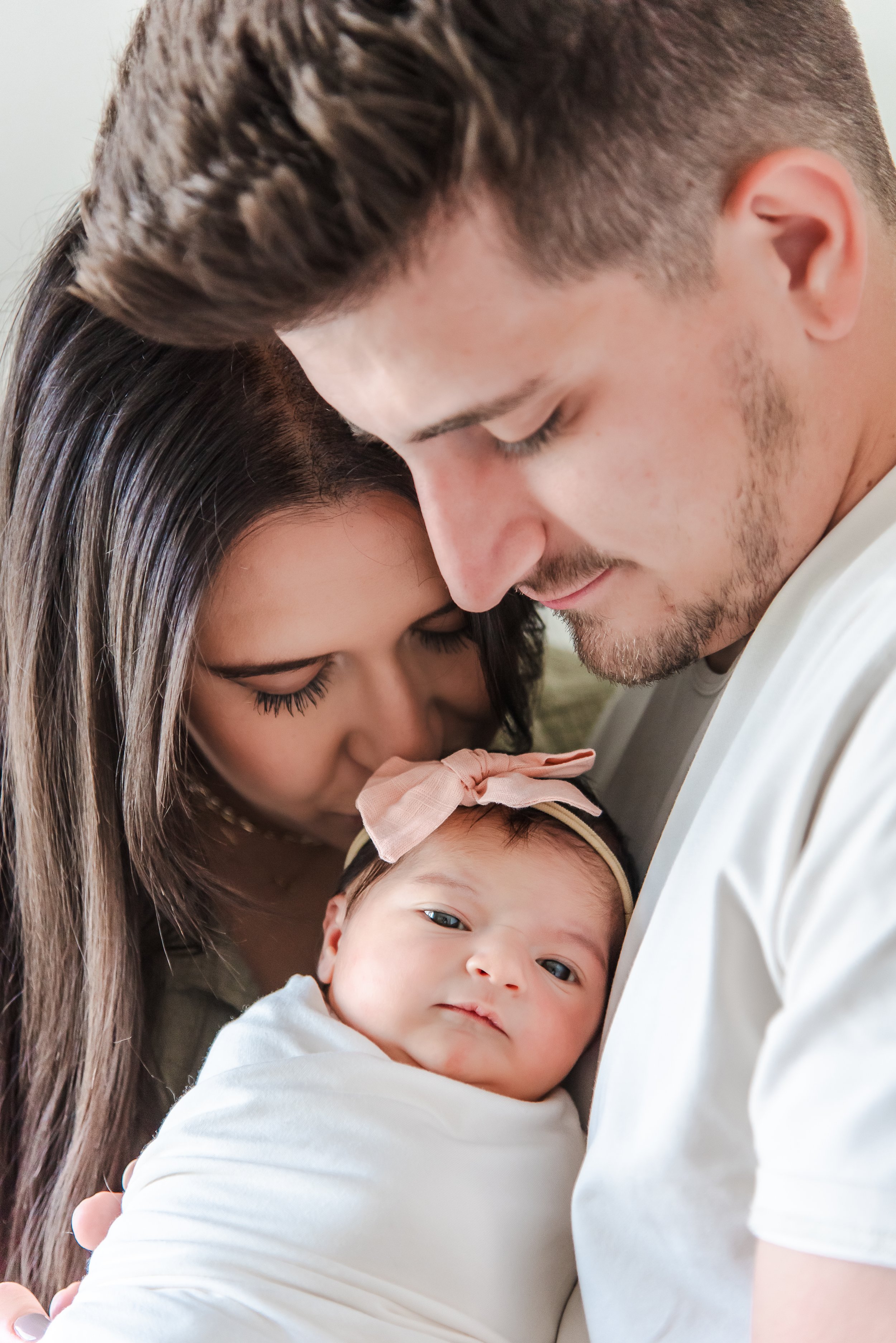 A young family, father, mother, and their newborn baby, with the parents gently holding and kissing the baby.