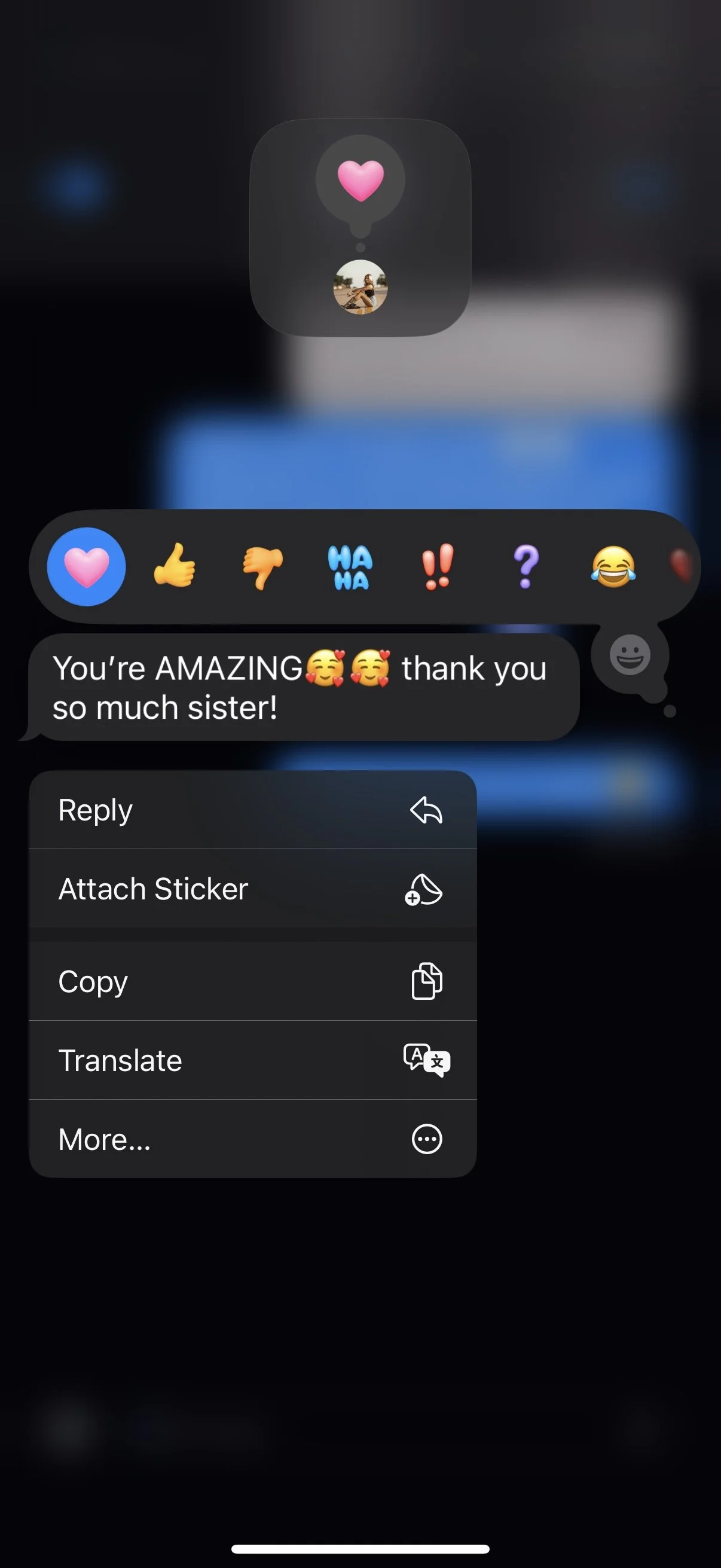 A smartphone screen displaying a messaging app where a message reads, "You're AMAZING🥰🥰 thank you so much sister!" The interface shows various reaction emojis including a heart, thumbs up, thumbs down, laughter, question mark, and laughing face. A context menu with options like reply, attach sticker, copy, translate, and more is open.