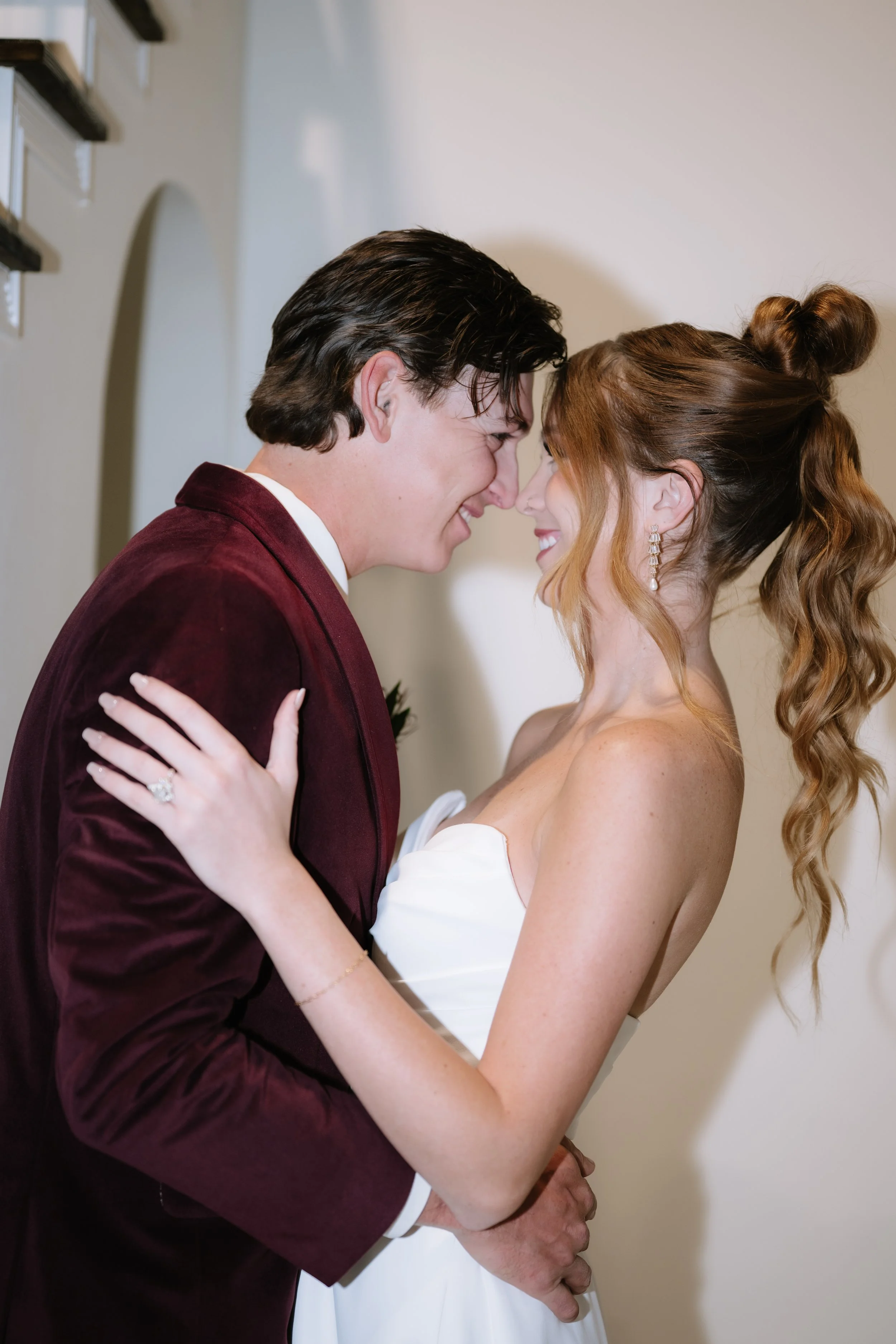 A bride and groom standing together outdoors near a lake, dressed in wedding attire on a cloudy day.
