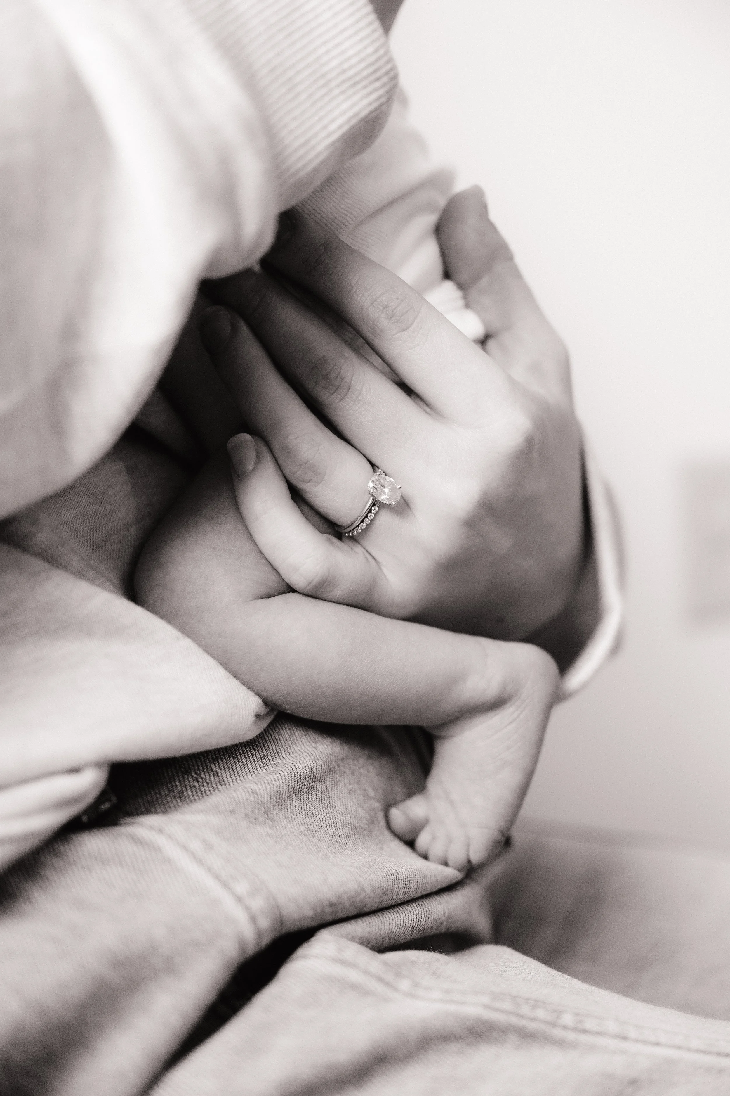 A man and pregnant woman sitting on the grass in a field, smiling, with tall dry grass and a cloudy sky in the background.