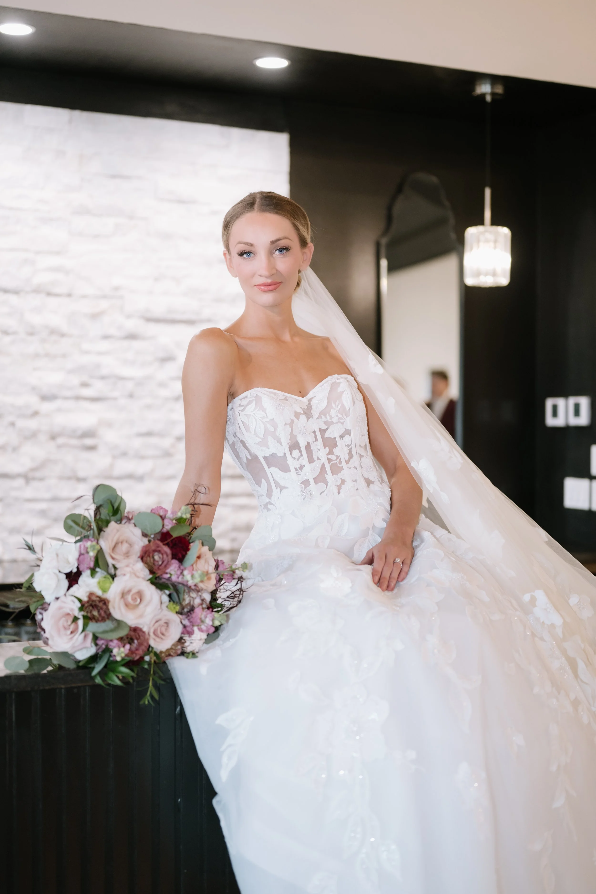 Bride in a white wedding dress and veil standing on staircase in an indoor setting.