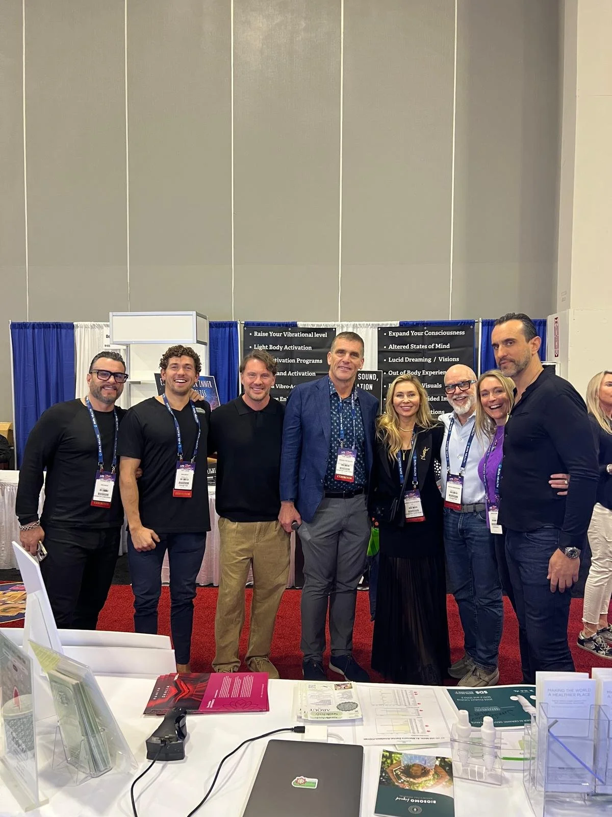 Group of people standing together at a conference or expo booth, smiling for the camera.