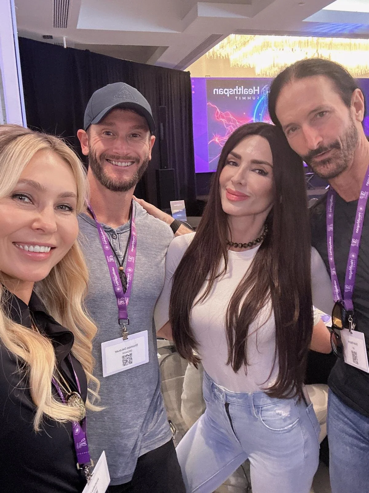 Group of four people smiling at a conference with a large presentation screen in the background.