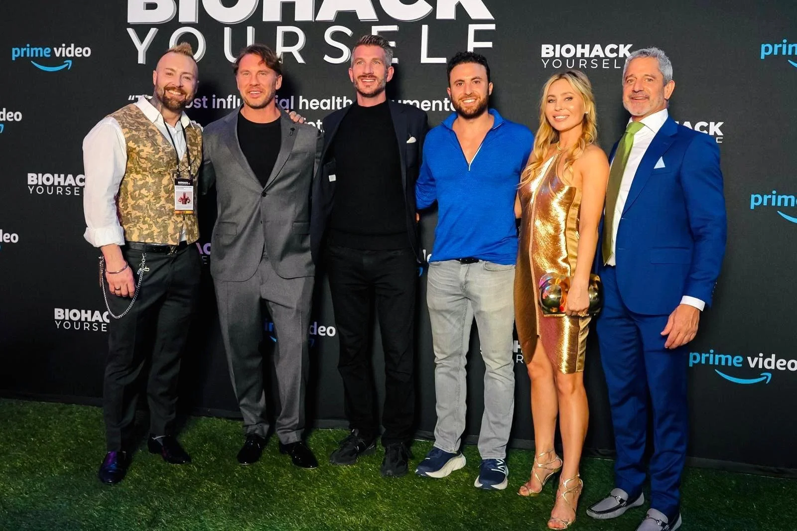 Seven people standing in front of a black backdrop with logos, dressed in formal and casual attire, smiling at the camera.
