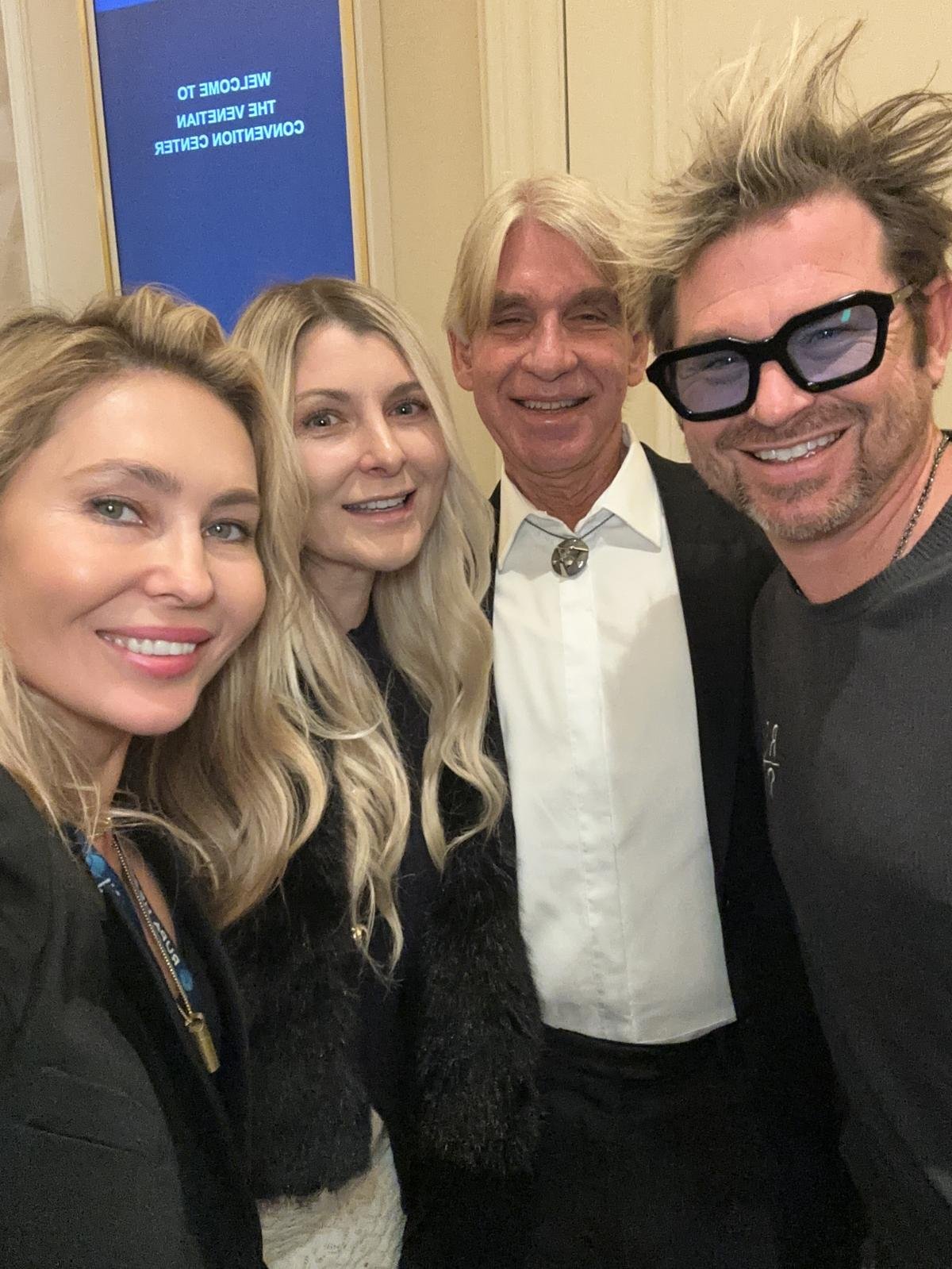 A group of four smiling people taking a selfie in front of a blue sign that says 'Welcome to the 37th Venice Conference Center'.