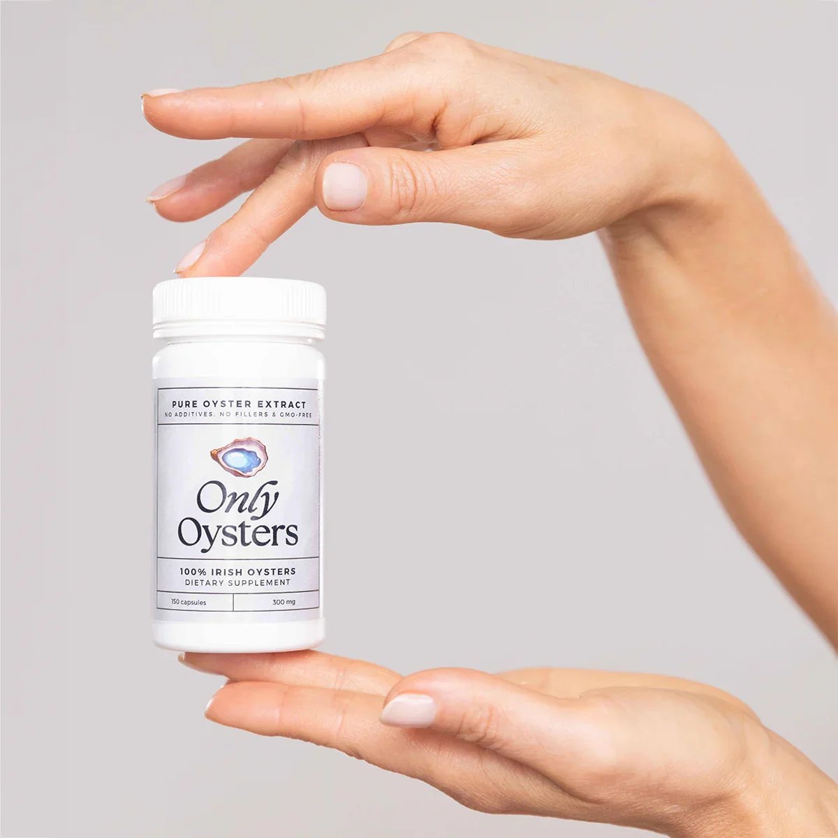 A hand holding a white bottle labeled 'Only Oysters' with a picture of an oyster, indicating dietary supplements made from Irish oysters.