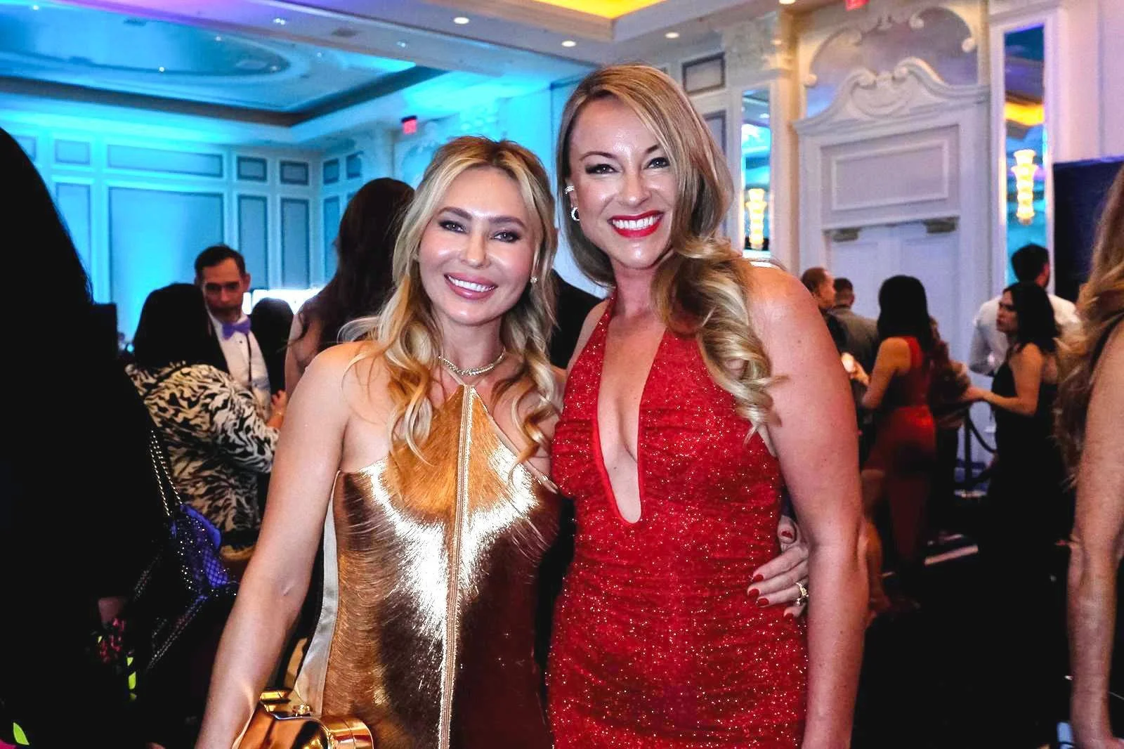 Two women in glamorous evening dresses smiling at a formal event.
