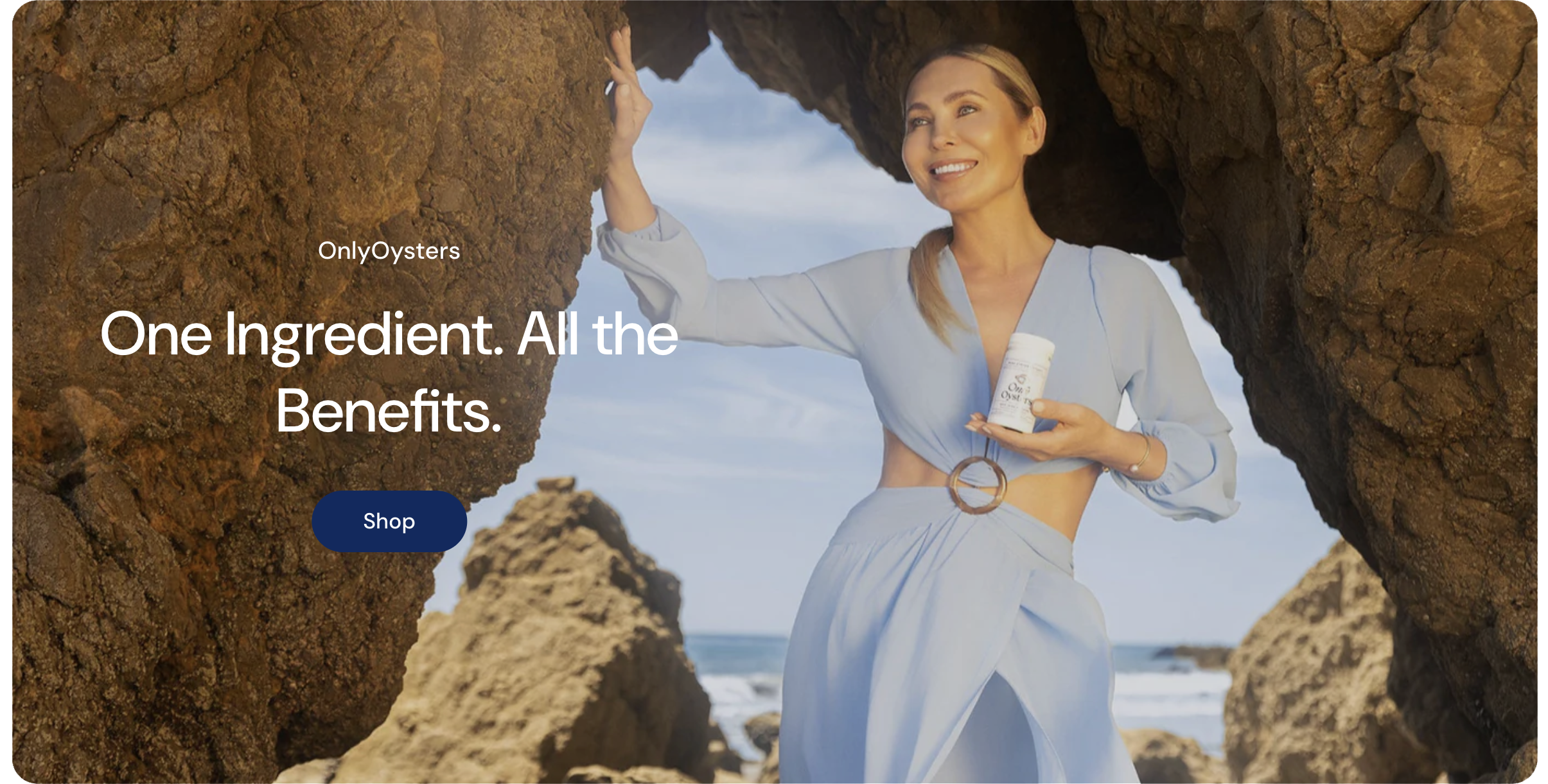 A woman in a light blue outfit stands between rocks on a beach, holding a bottle of dietary supplement with sea in the background.