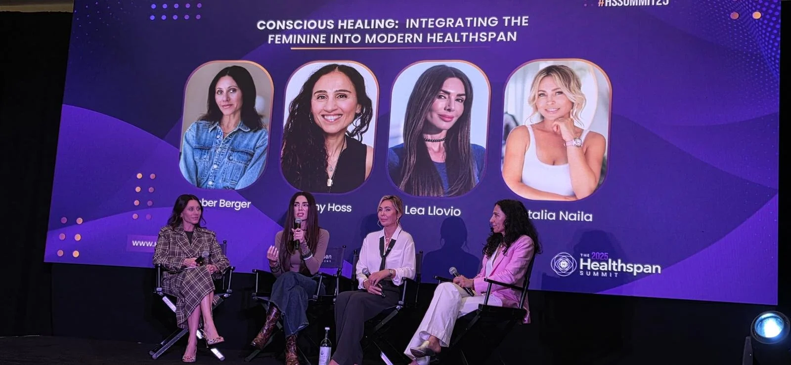 Panel discussion at the Healthspan Summit 2025 on the topic of conscious healing and integrating the feminine into modern health span, featuring four women speakers seated on stage and a large screen behind them displaying photos and names of four fe