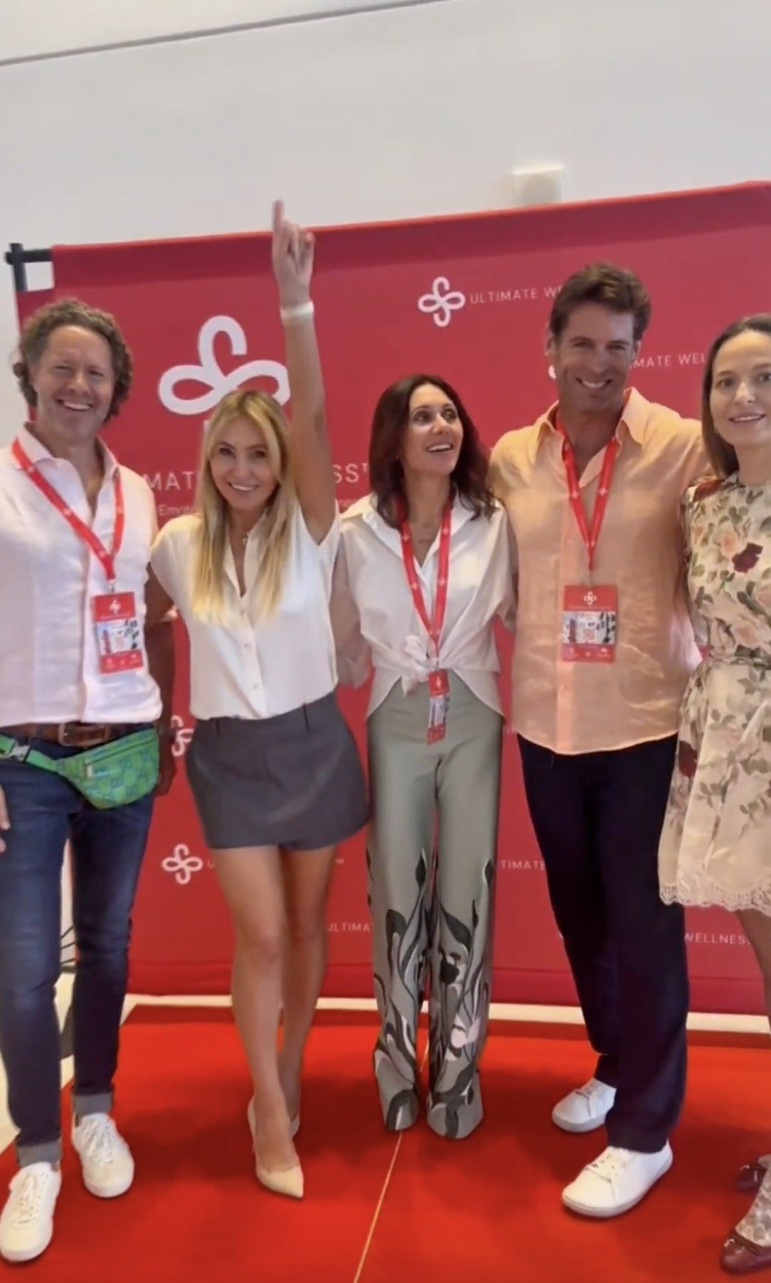 Group of five people standing together at an event, smiling, with a red backdrop behind them that has white text and logos.