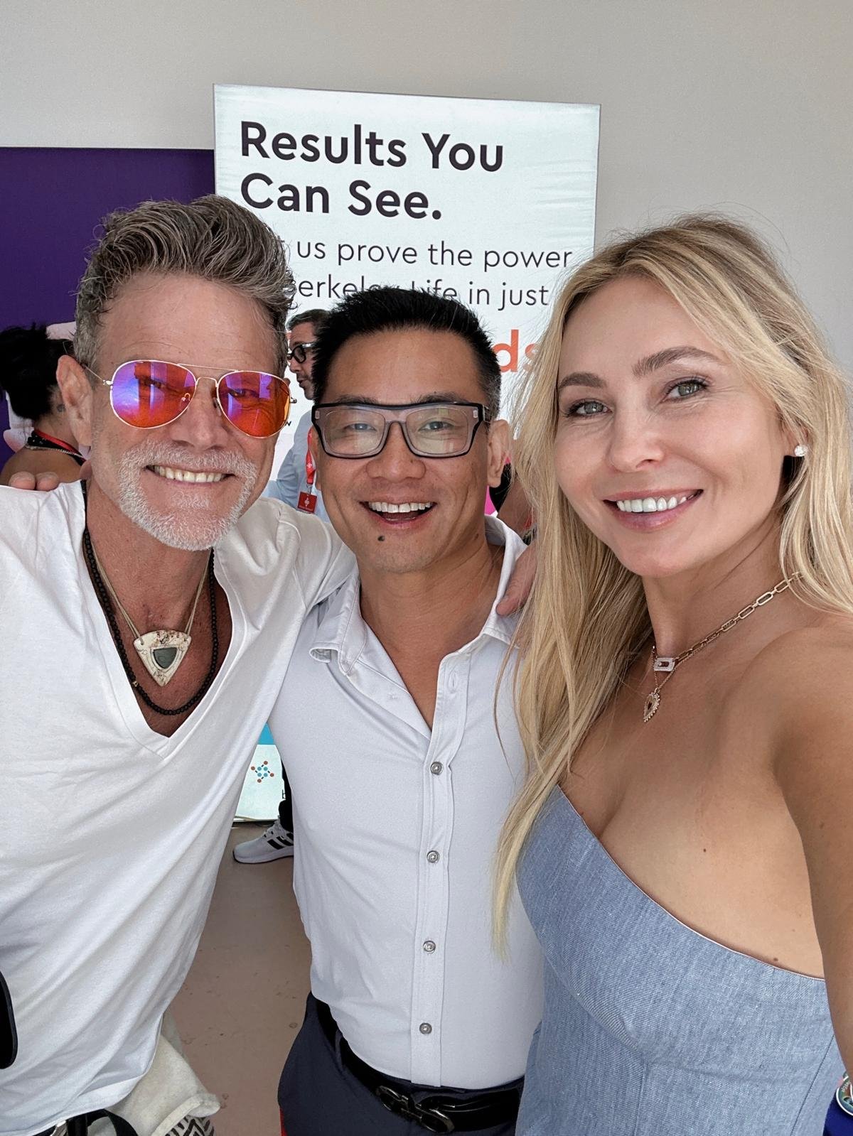 Three people smiling for a photo at an event. The background has a sign with the text 'Results You Can See. proves the power in just.'