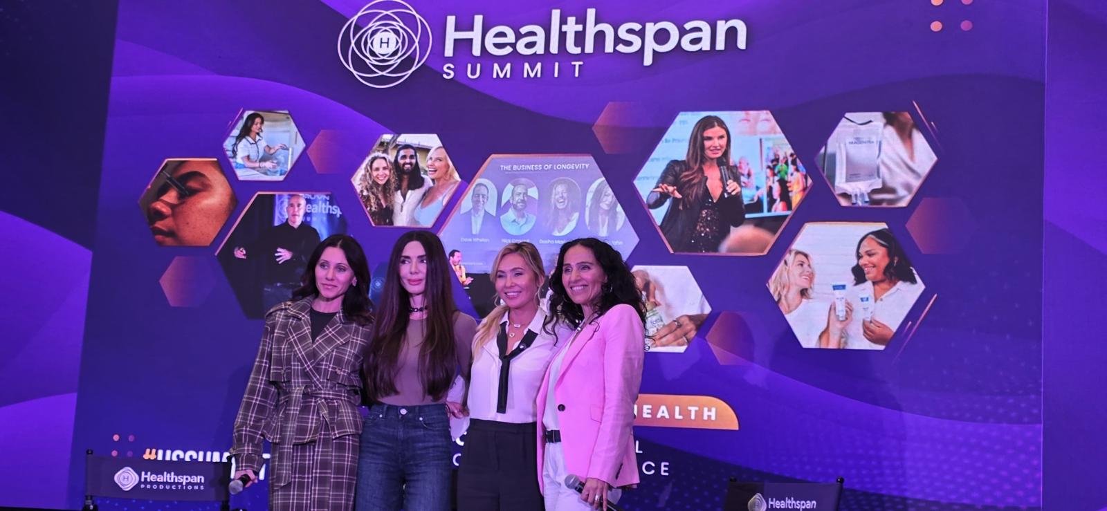 Four women standing together on stage at the Healthspan Summit, smiling, with a purple backdrop featuring hexagonal images of healthcare-related scenes and the Healthspan logo.
