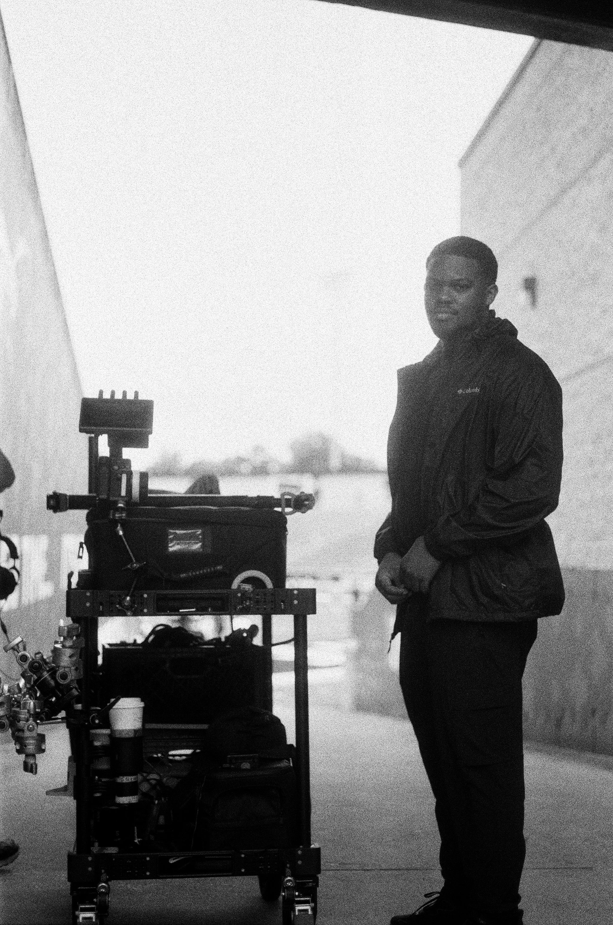 A man standing next to a cart with scientific or camera equipment, outdoors in an overcast or foggy environment.