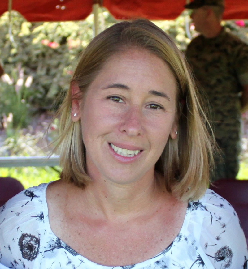 A woman with blonde hair smiles outdoors at Mountain View Veterinary Hospital, with another person and greenery in the background.