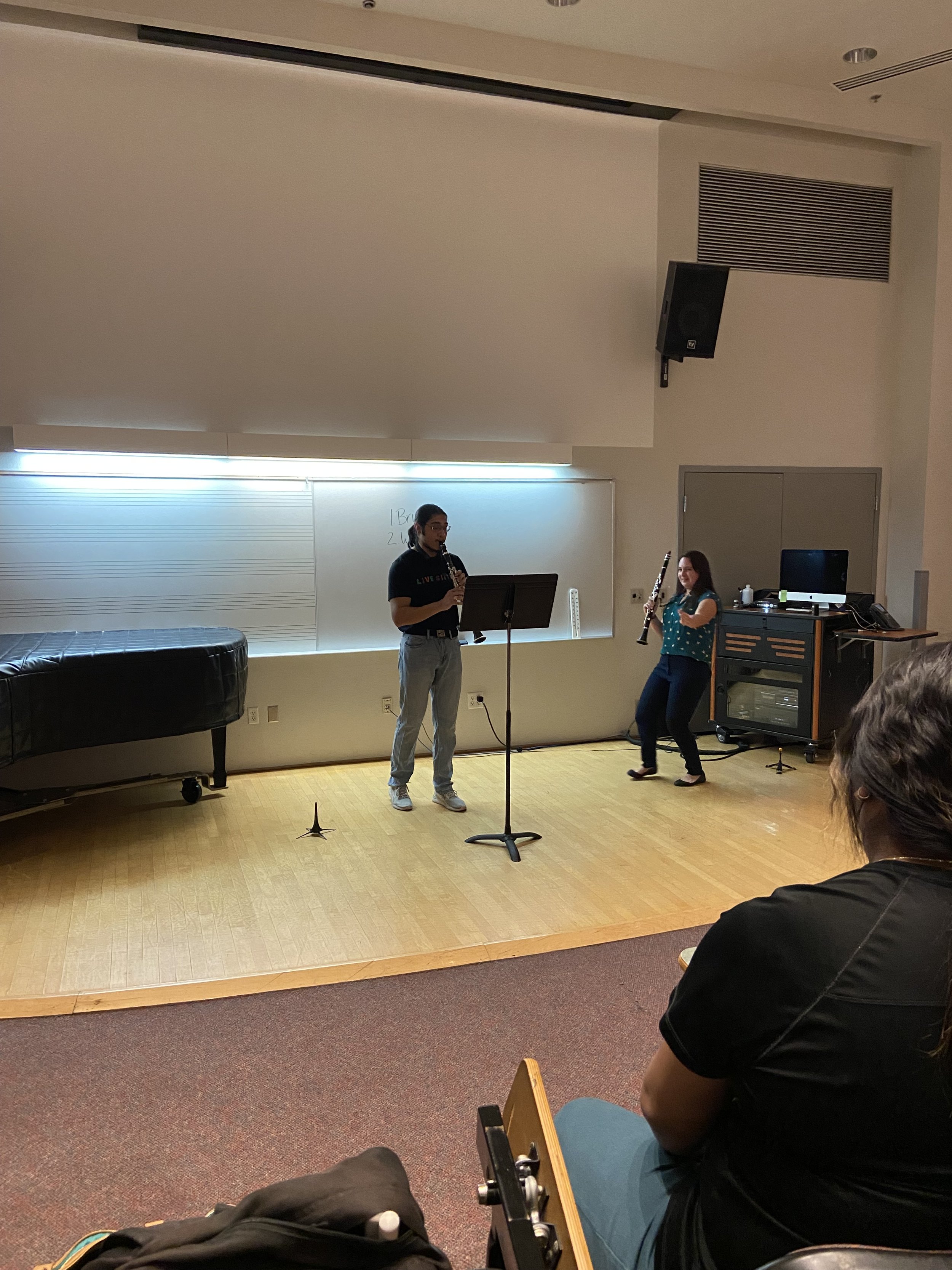 A classroom performance with two musicians playing wind instruments, a man and a woman, while an audience watches.