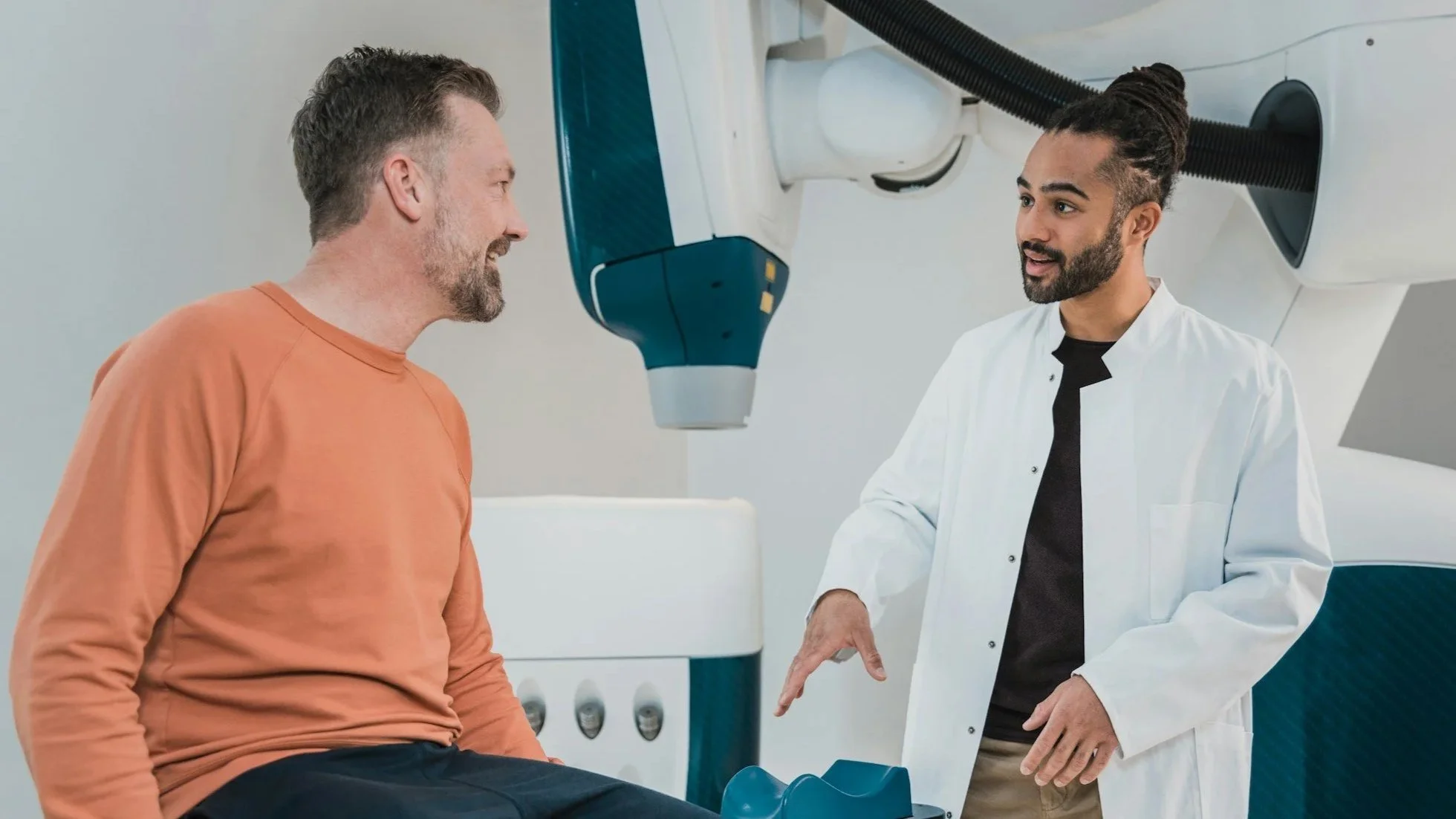 A doctor explaining a medical procedure to a middle-aged man in an MRI room.