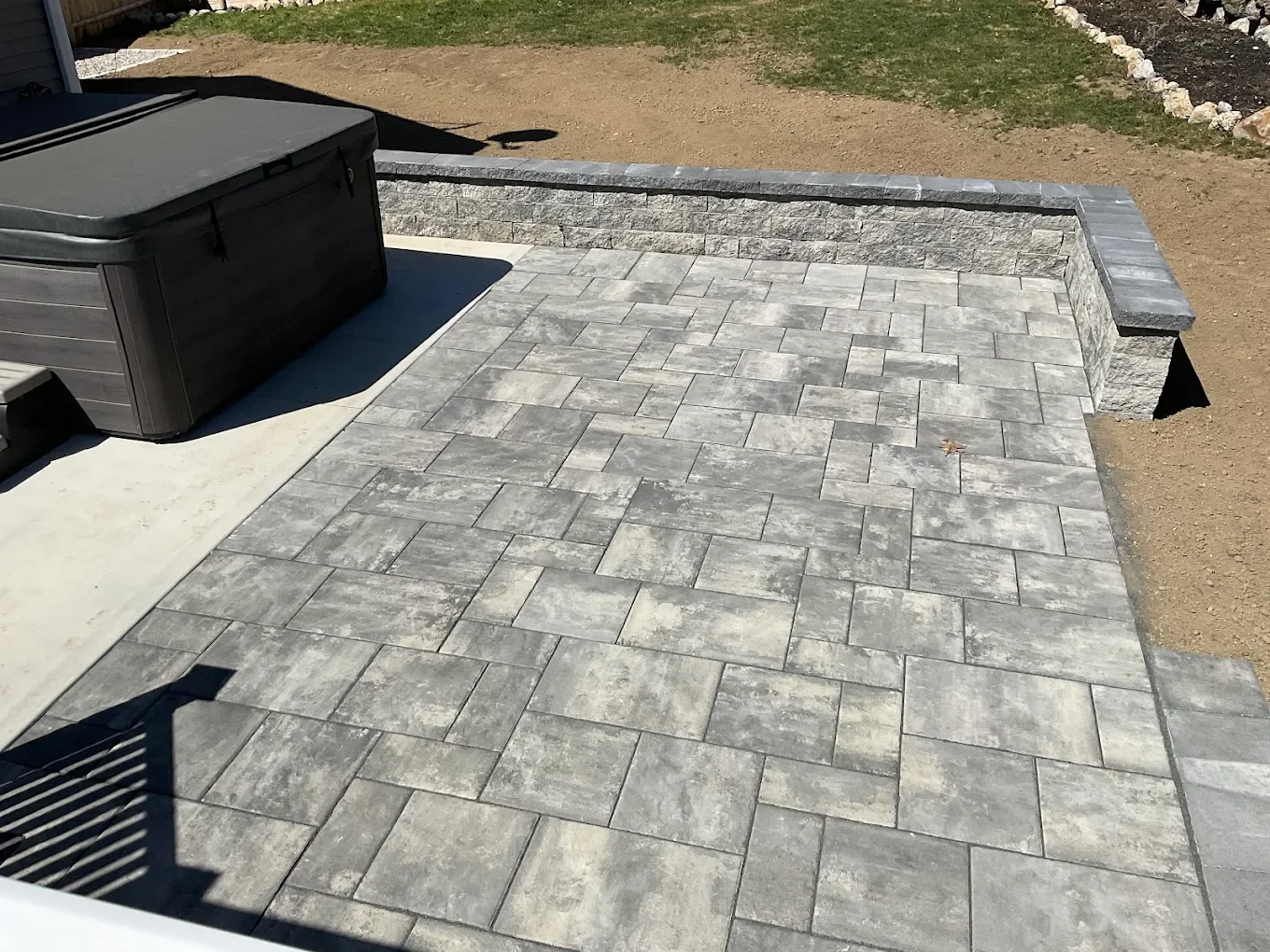 Newly installed backyard patio with light gray pavers and wooden deck stairs, showing clean modern lines.