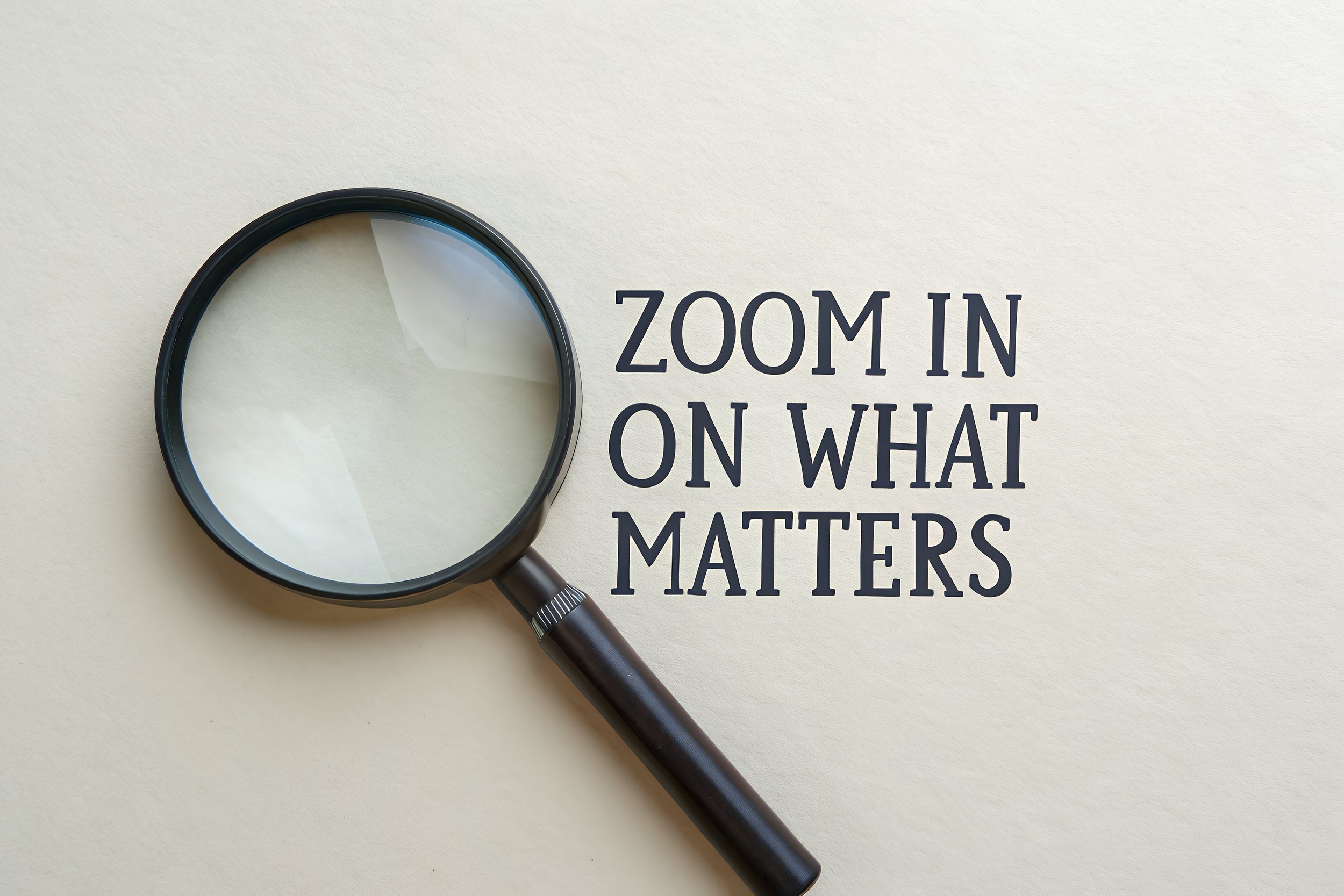 A magnifying glass placed on a light-colored surface, with the words 'Zoom in on what matters' written next to it.