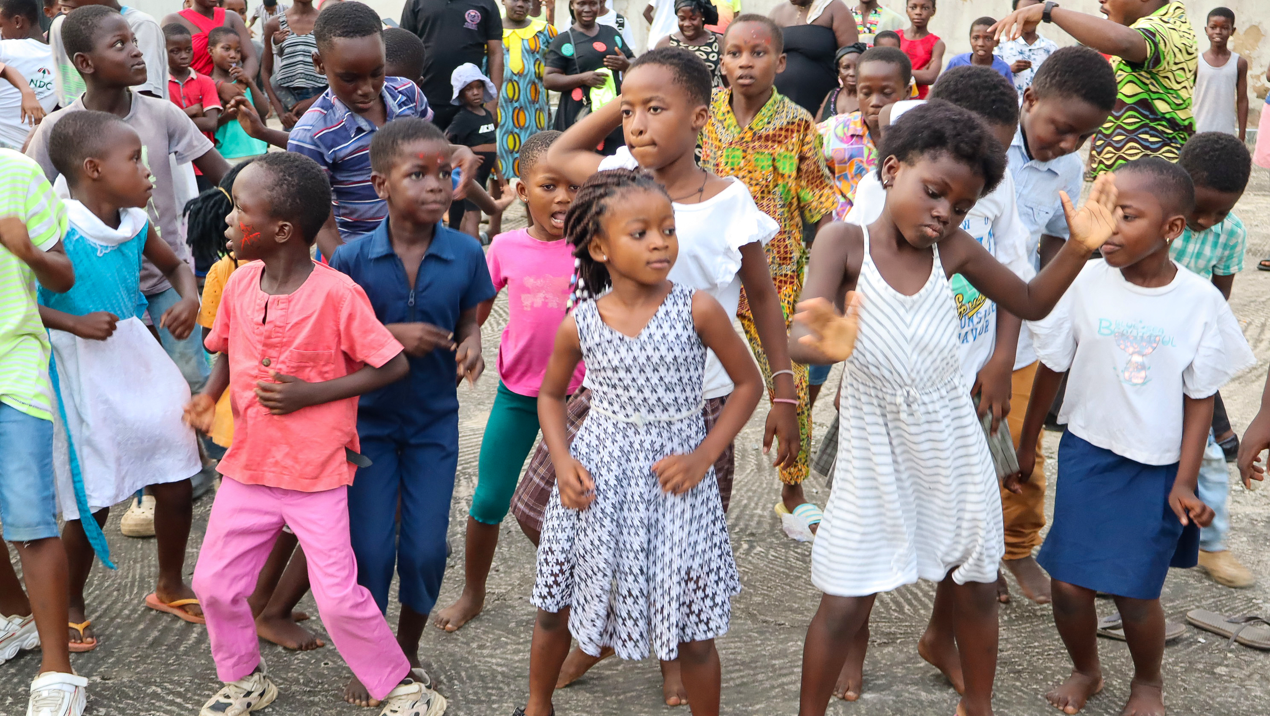 Group of children dancing and playing outdoors in a community gathering.