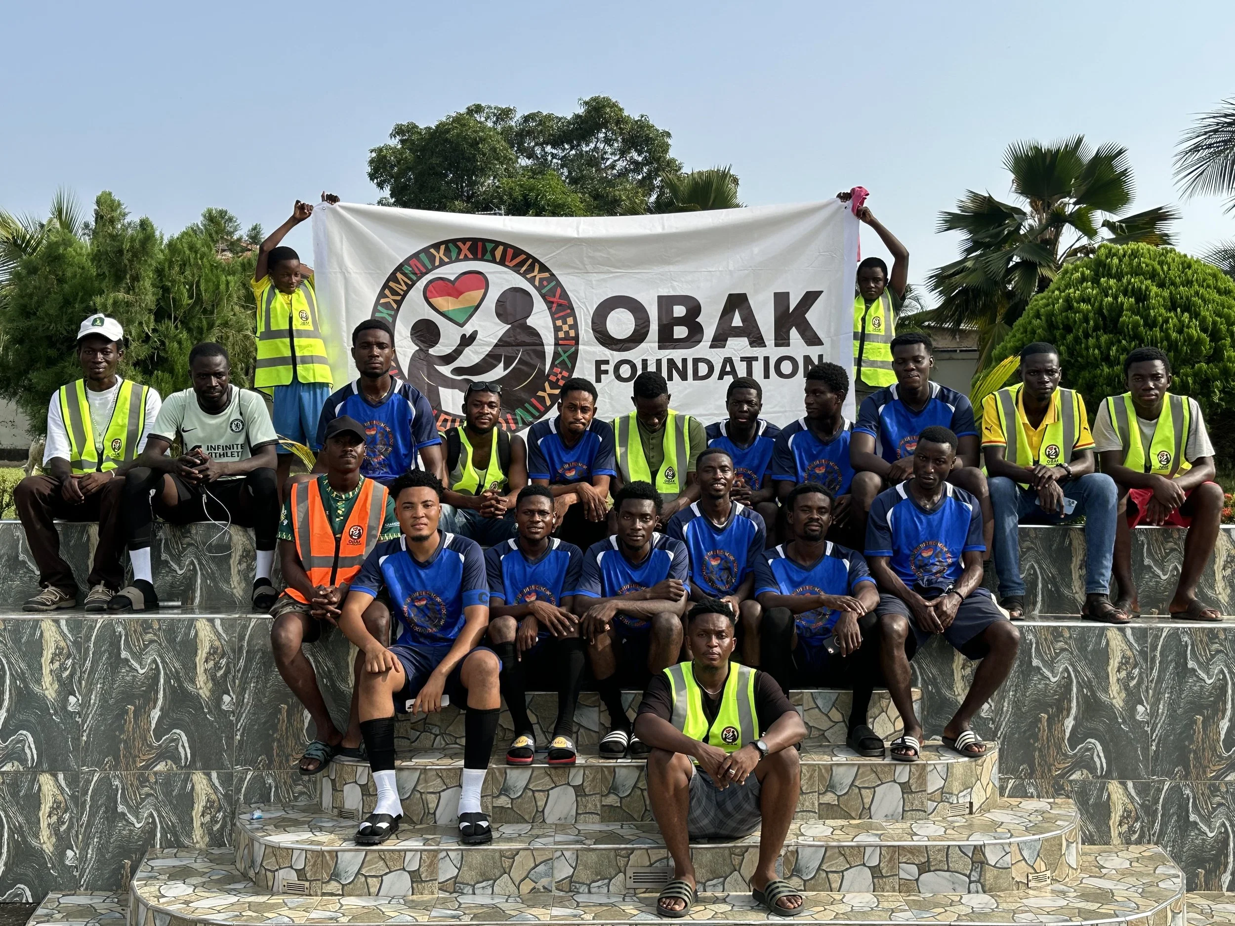 Group of young men posing outdoors with a banner reading 'OBAK Foundation.'