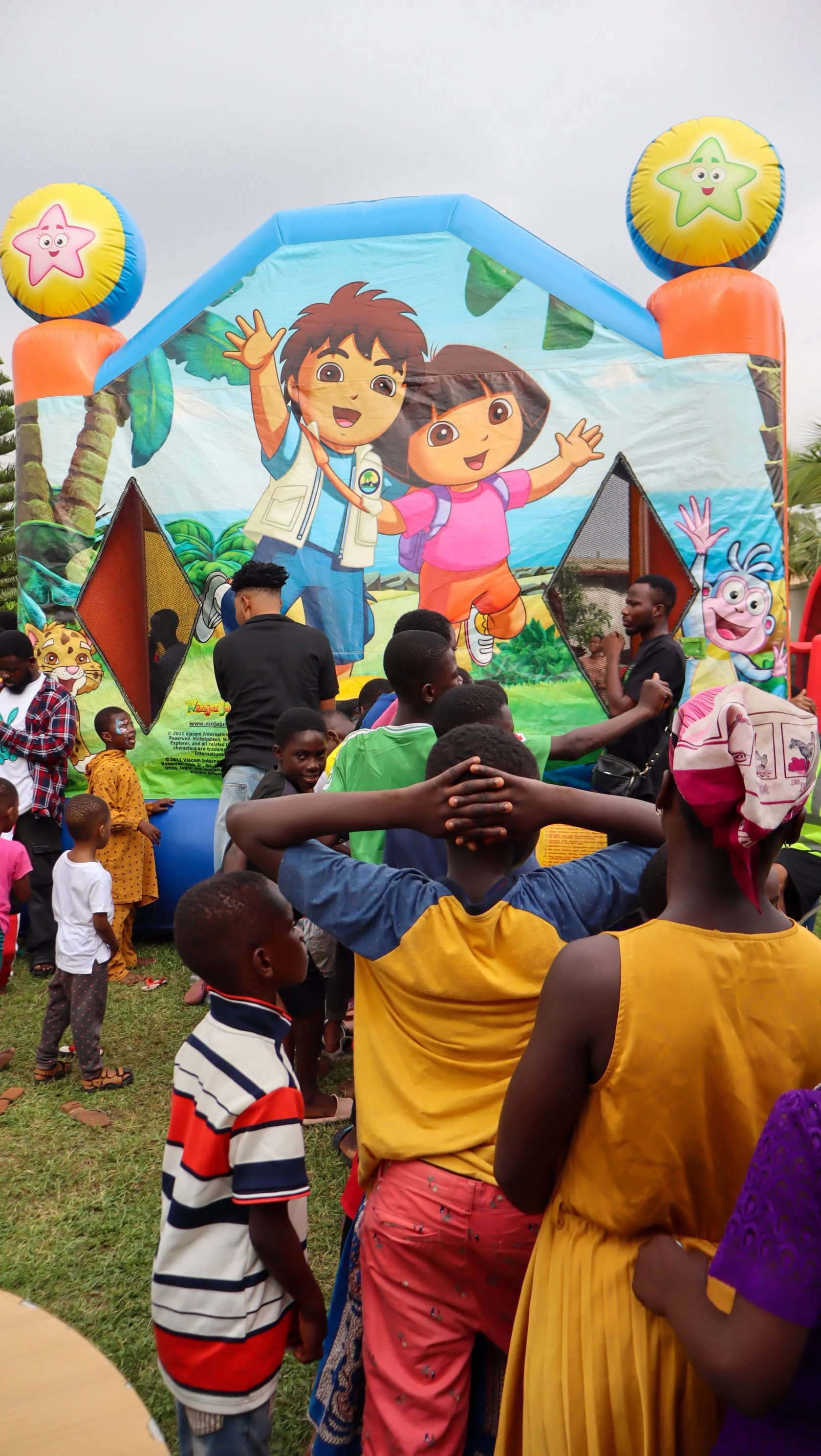 Children gathered at an outdoor event with a colorful inflatable bounce house featuring cartoon characters from 'Dora the Explorer'.