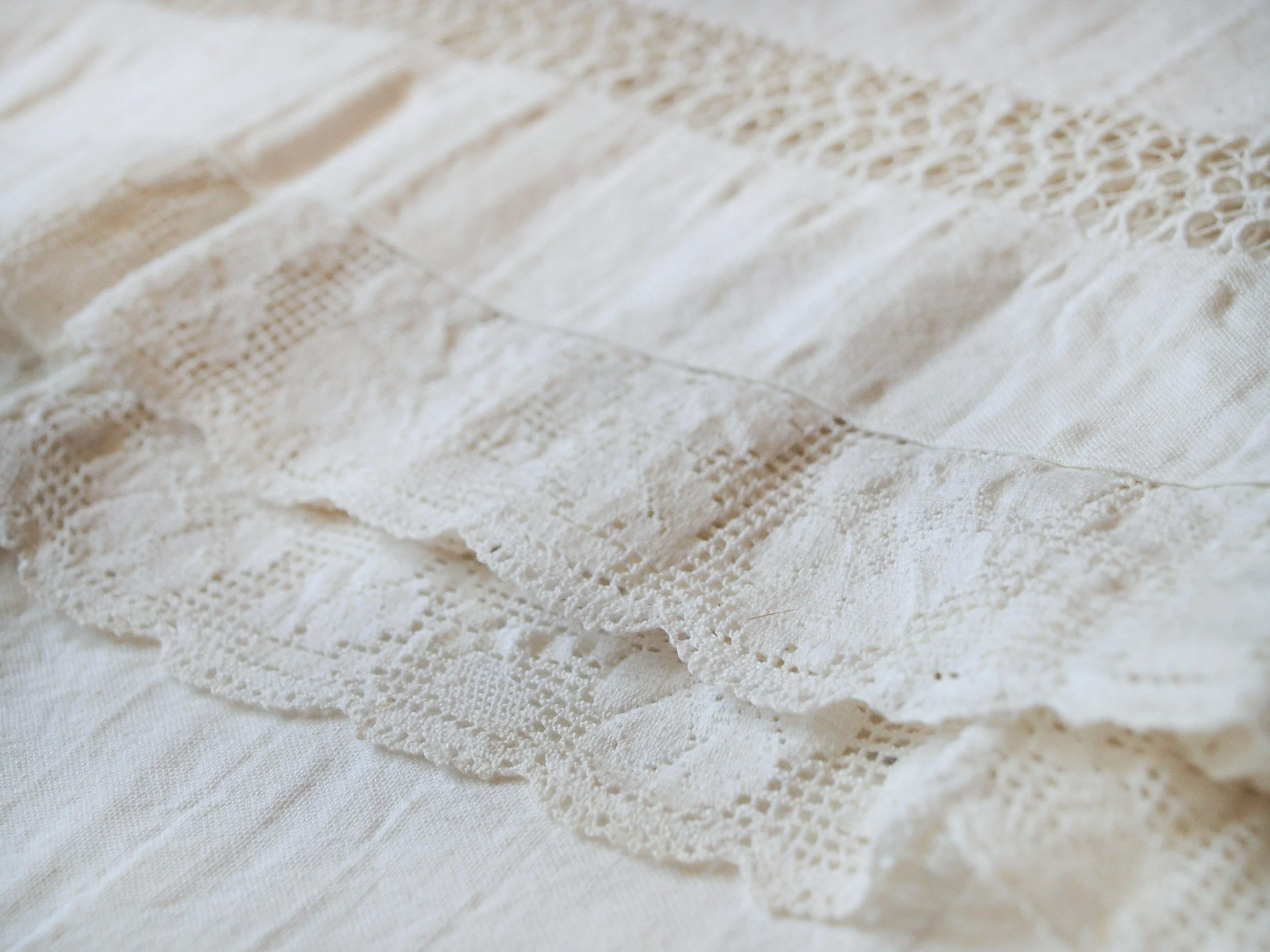 Close-up of a white lace fabric with intricate crochet and woven patterns, laid flat on a surface.