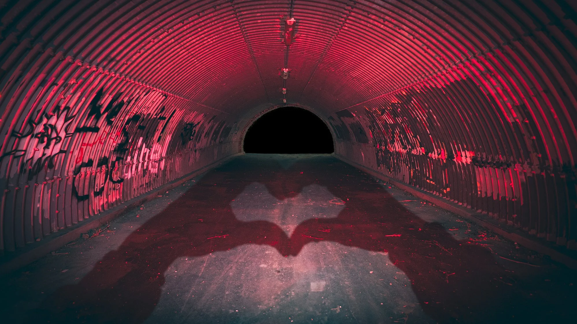Dark tunnel with red lighting and graffiti on the walls, leading into an unlit black opening