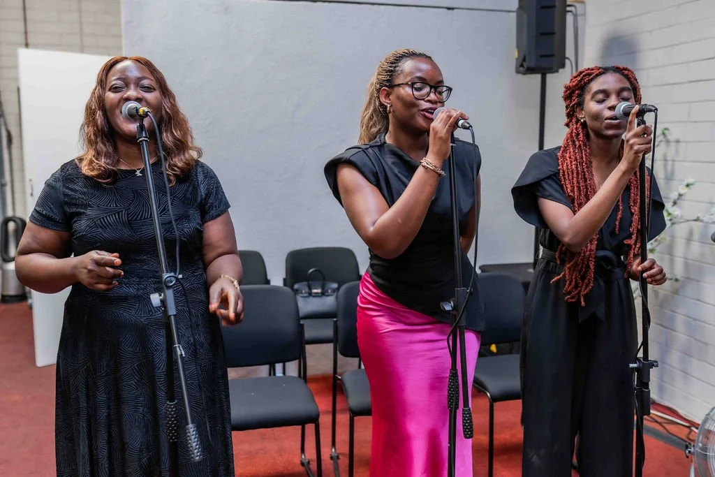 Three women singing into microphones at an indoor event
