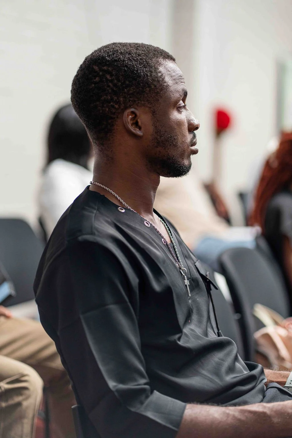Black man seated in profile wearing a black shirt and layered cross necklaces