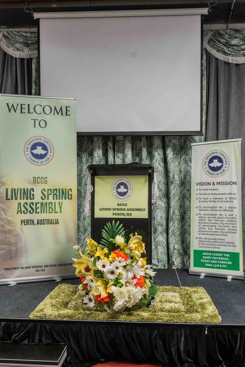 Church stage with a projection screen, pulpit, floral arrangement, and banners for Redeemed Christian Church of God Living Spring Assembly in Perth, Australia