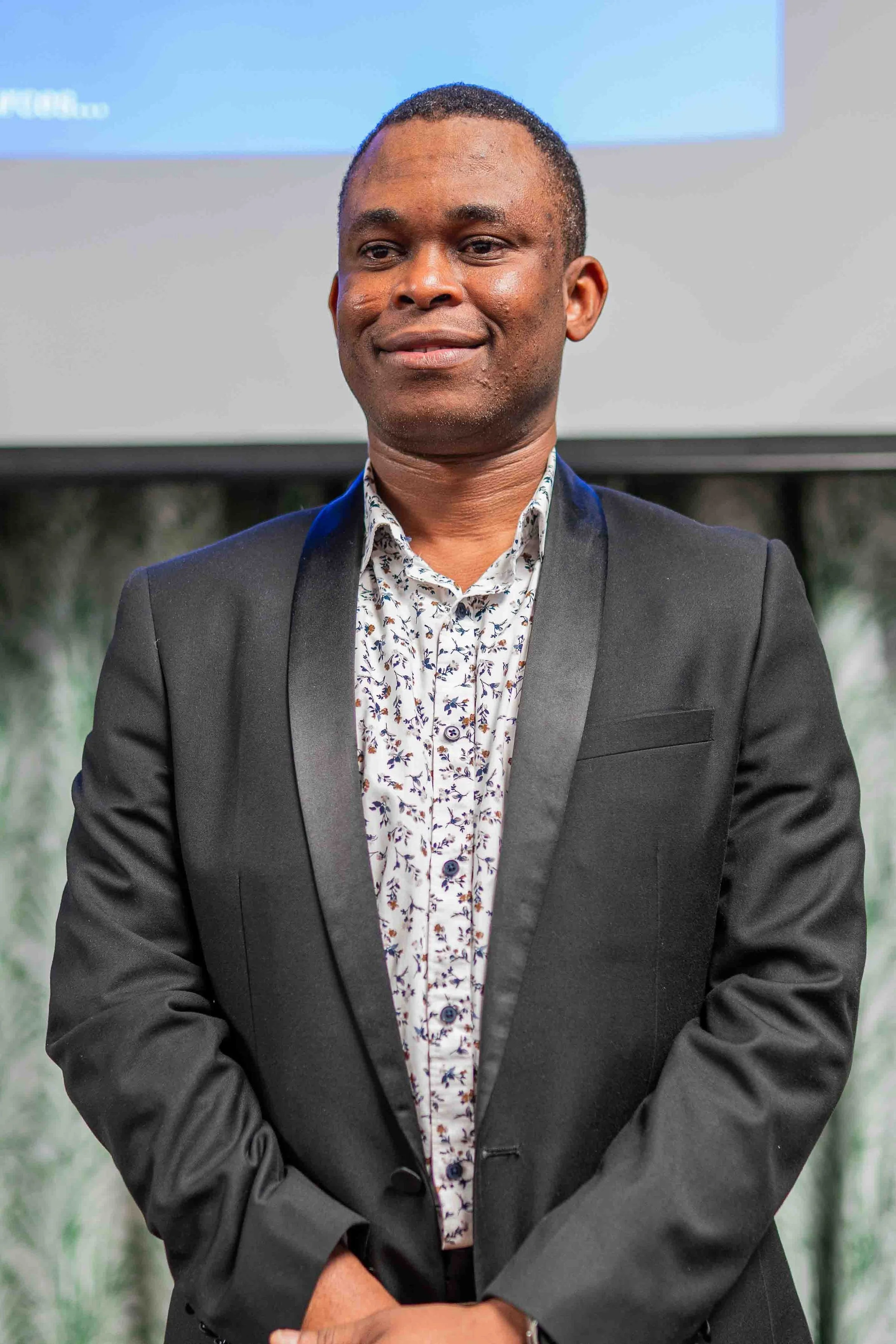 Portrait of a smiling Black man wearing a gray suit jacket and floral shirt indoors