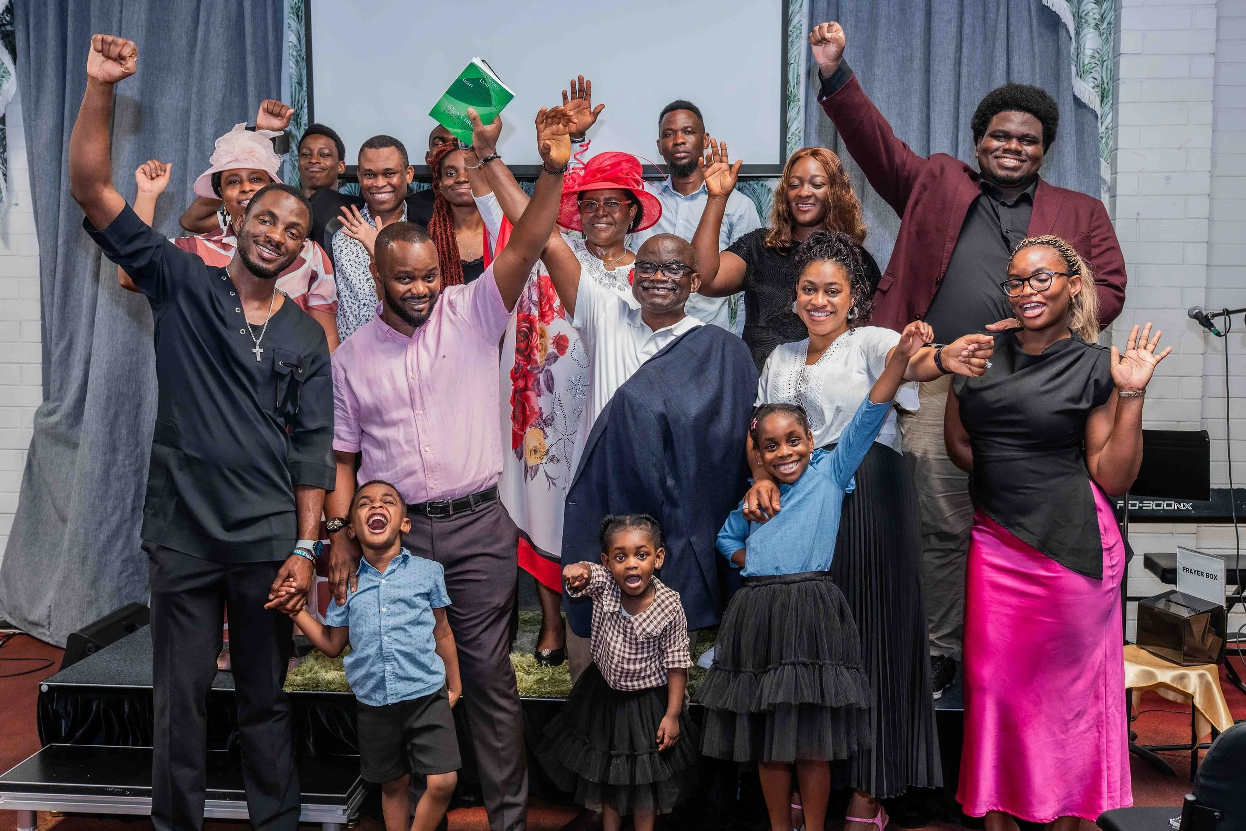 Multigenerational church congregation posing on stage with raised hands, children, and worship decorations