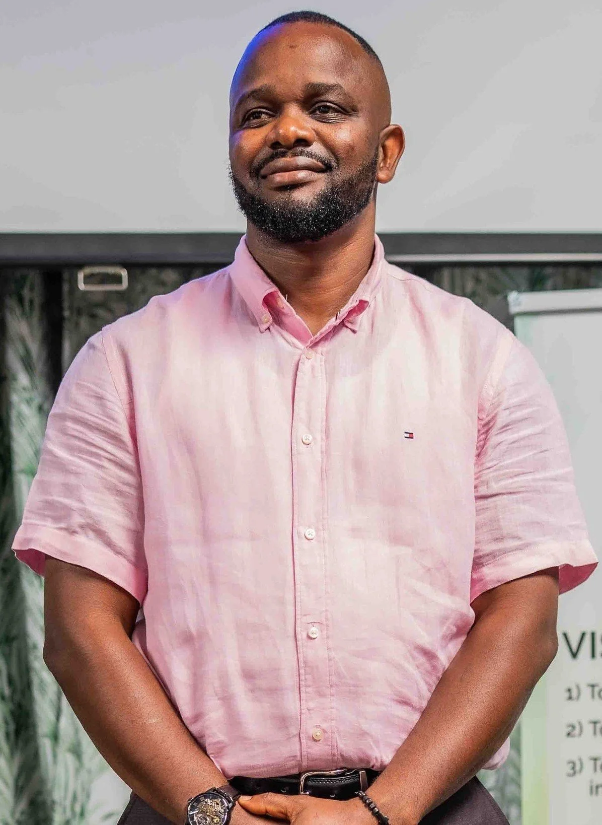 Portrait of a bearded man in a pink button-down shirt standing with his hands clasped