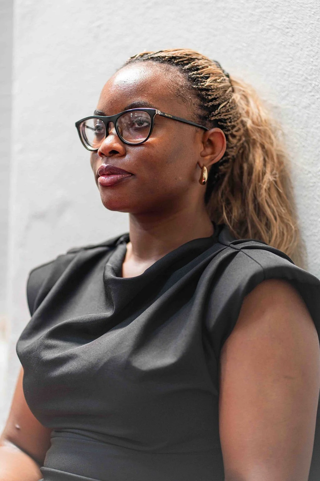 Portrait of a Black woman wearing black glasses, gold hoop earrings, and a sleeveless black top