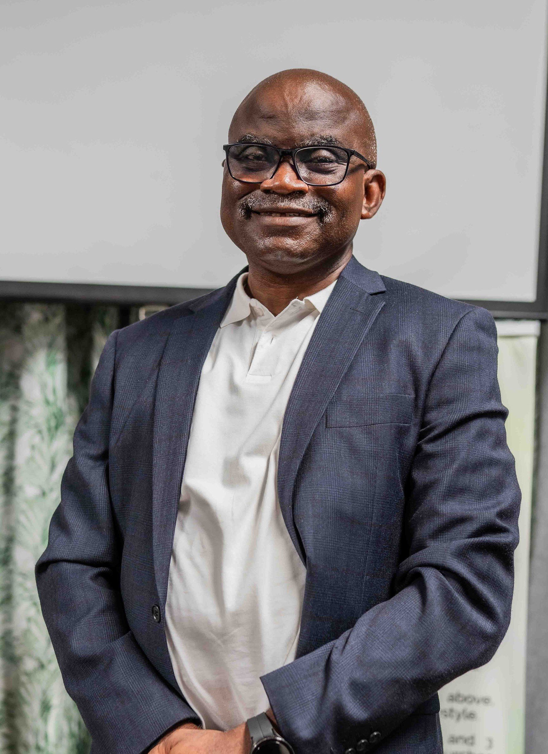 Portrait of a bald Black man wearing glasses, a navy blazer, and a white shirt