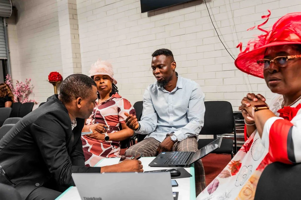 Group of people in colorful attire talking around laptops in a meeting room
