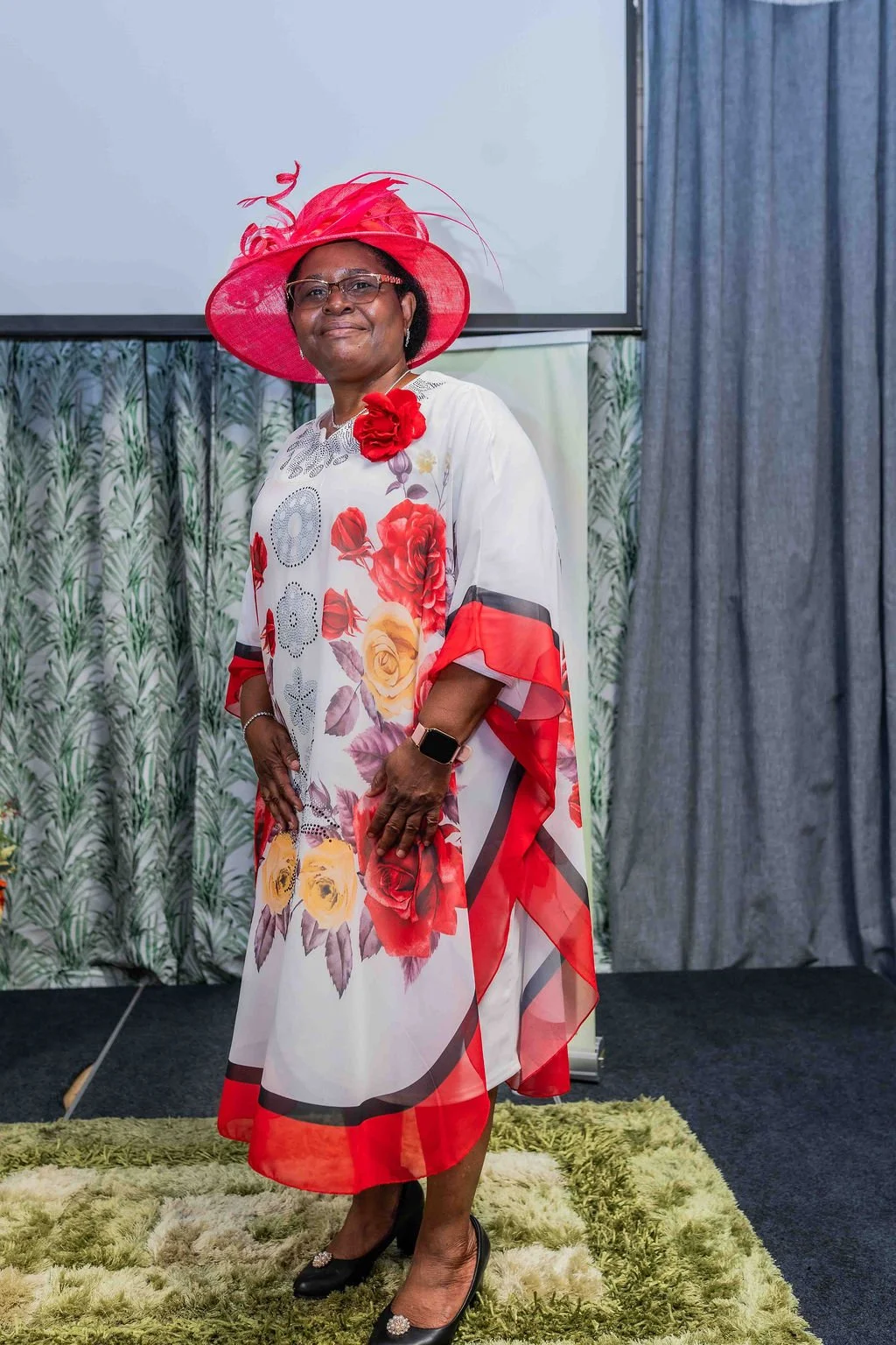 Woman wearing a red fascinator and floral dress posing indoors