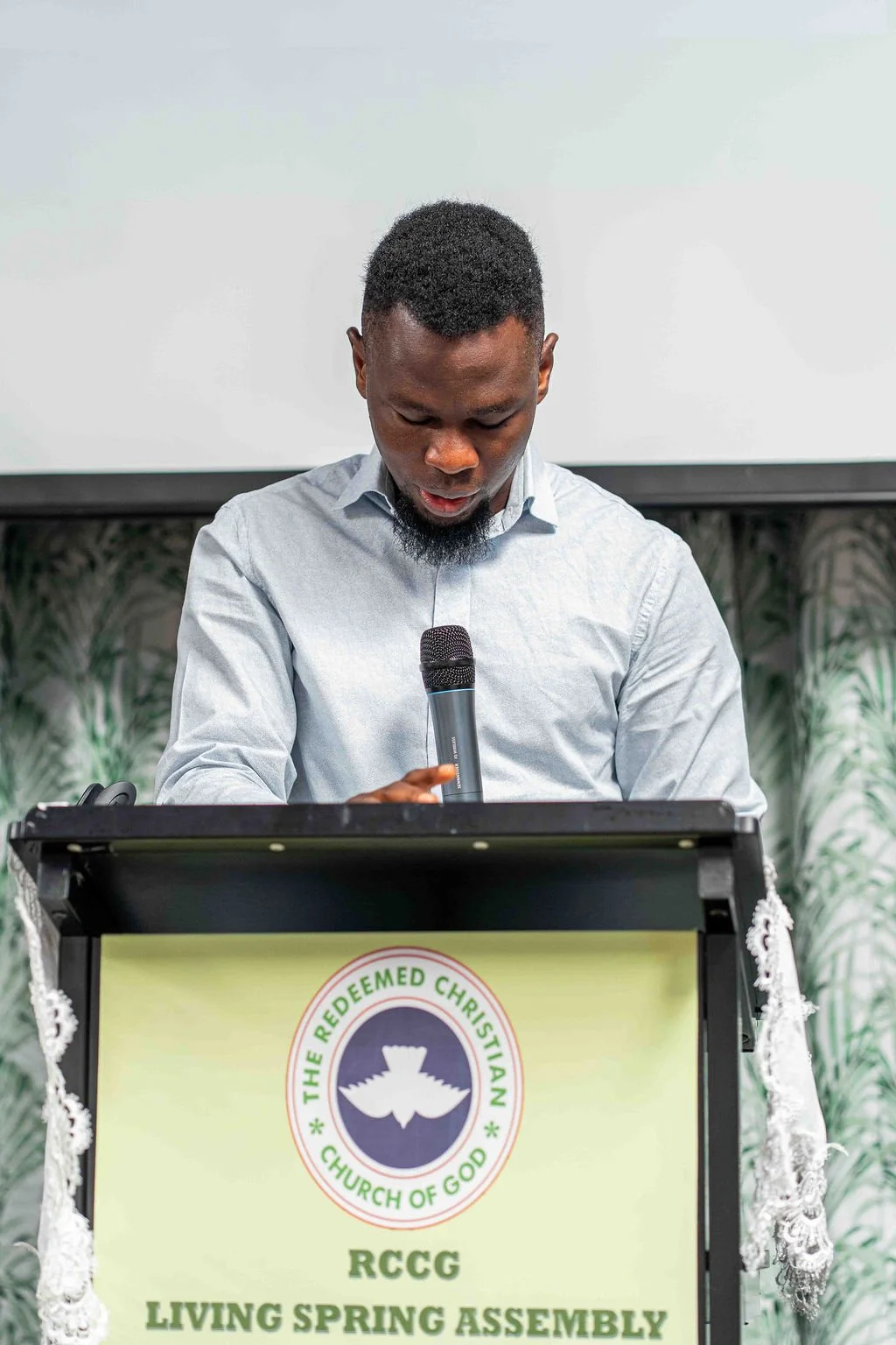 Man speaking into a microphone behind a podium at a Redeemed Christian Church of God service