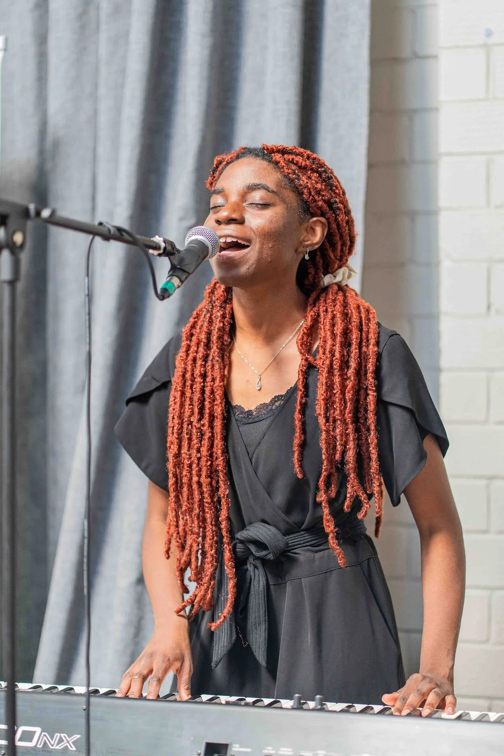 Singer with long red braids performing into a microphone while playing a keyboard