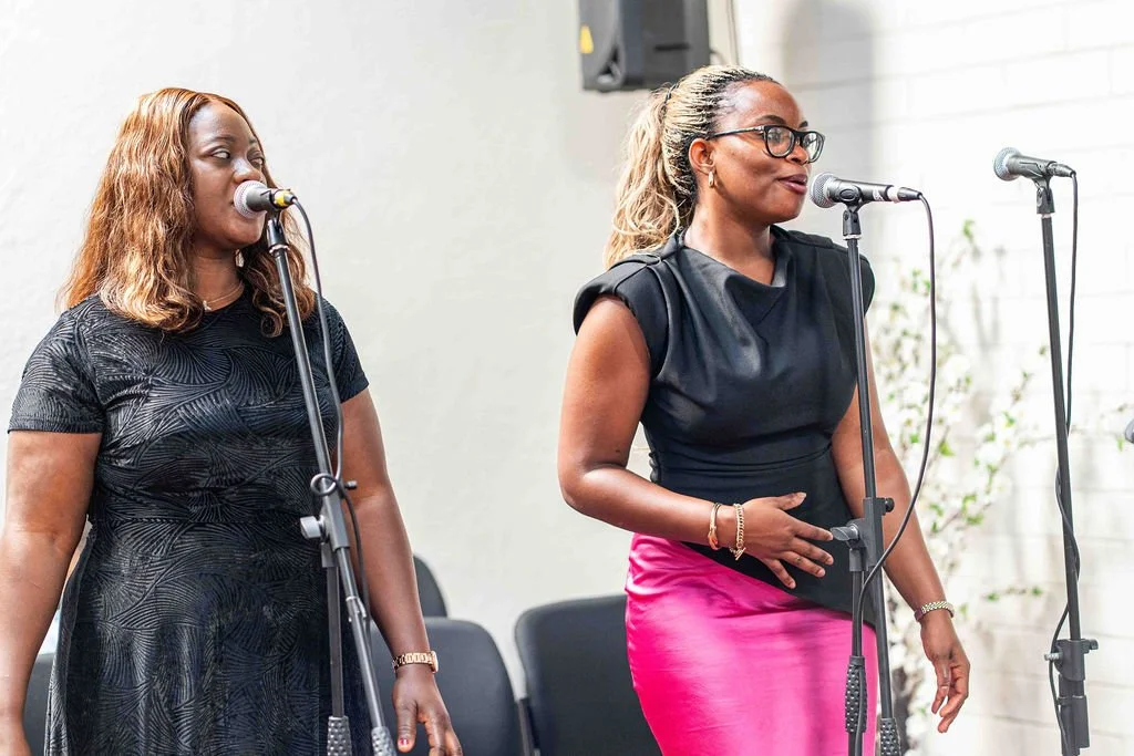 Two women singing into microphones during a live performance