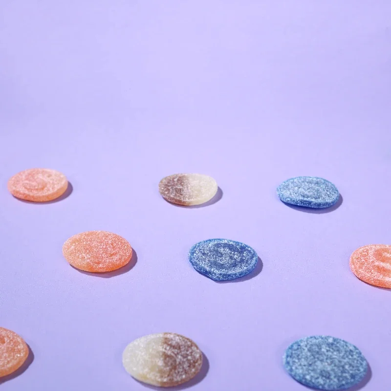 Assorted colorful Swedish S-Marke sour gummy candy in blue raspberry, peach and cola flavor.